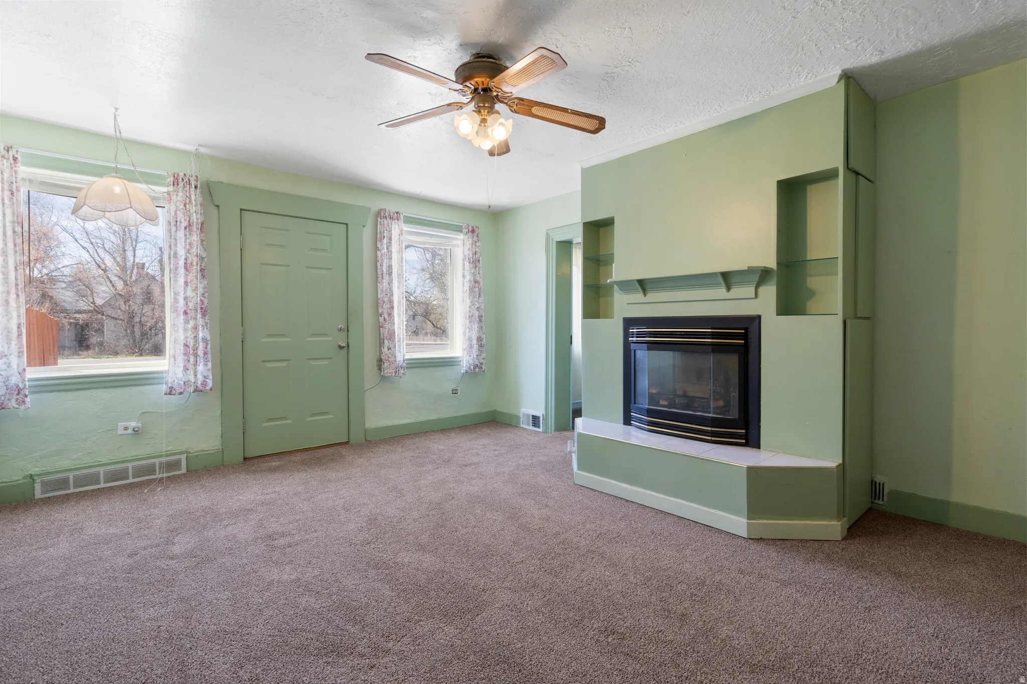 Unfurnished living room with ceiling fan, carpet flooring, a glass covered fireplace, and a textured ceiling