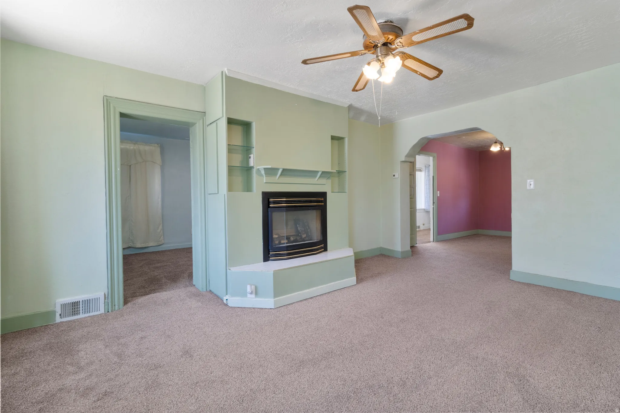 Unfurnished living room with a ceiling fan, carpet, a glass covered fireplace, a textured ceiling, and arched walkways