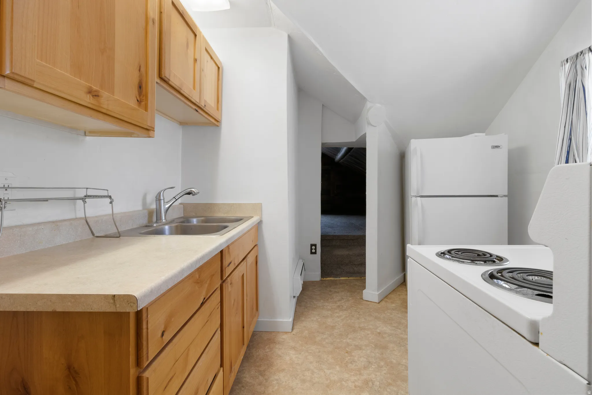 Kitchen featuring white appliances, light countertops, vaulted ceiling, and light wood finish cabinets
