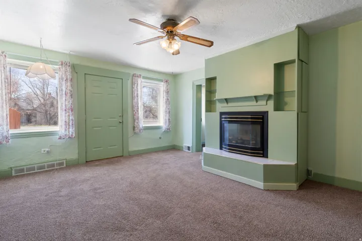 Unfurnished living room with ceiling fan, carpet flooring, a glass covered fireplace, and a textured ceiling