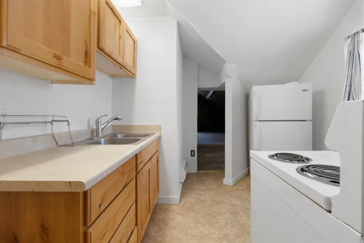 Kitchen featuring white appliances, light countertops, vaulted ceiling, and light wood finish cabinets