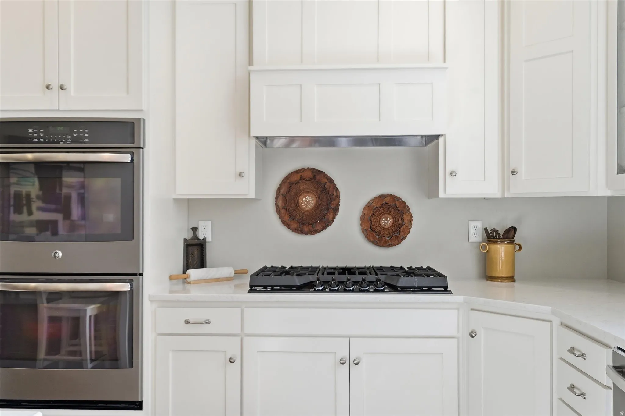 Kitchen with double oven, white cabinetry, and light stone counters