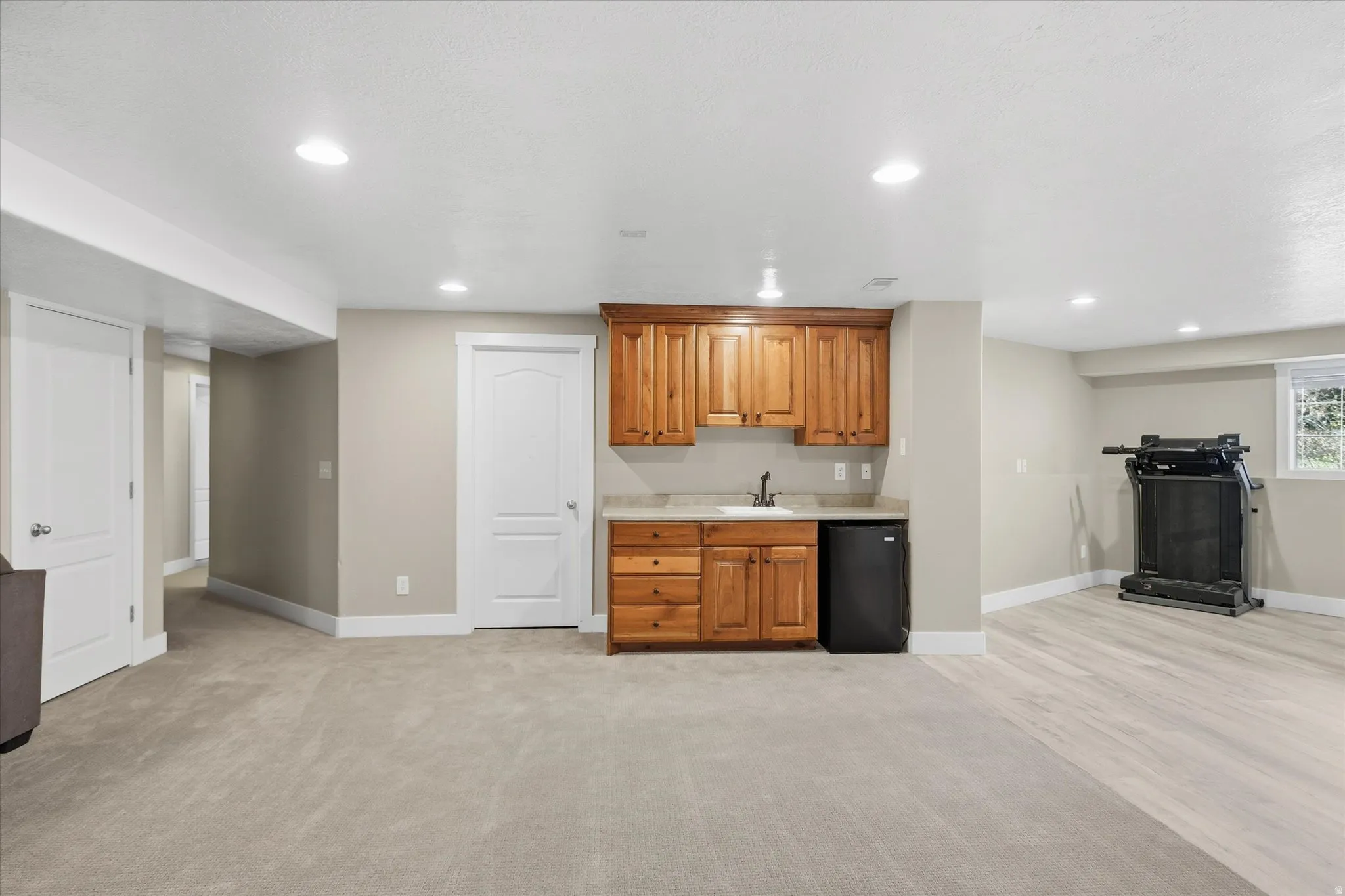 Indoor wet bar featuring wood finish cabinetry, black fridge, recessed lighting, and light carpet