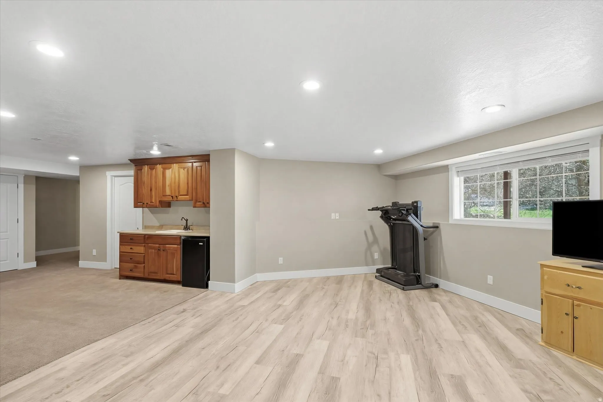 Exercise area with recessed lighting, light wood-style floors, and bar with sink