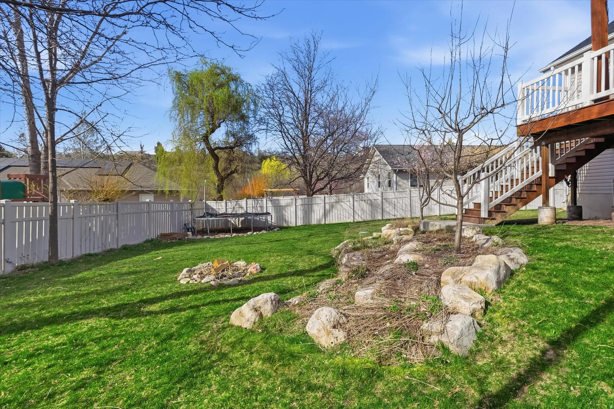 Fenced backyard with a trampoline, a fire pit, and a wooden deck