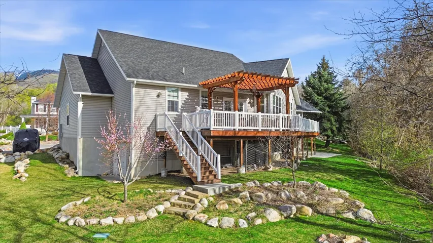 Back of house featuring roof with shingles, a wooden deck, a lawn, and a pergola
