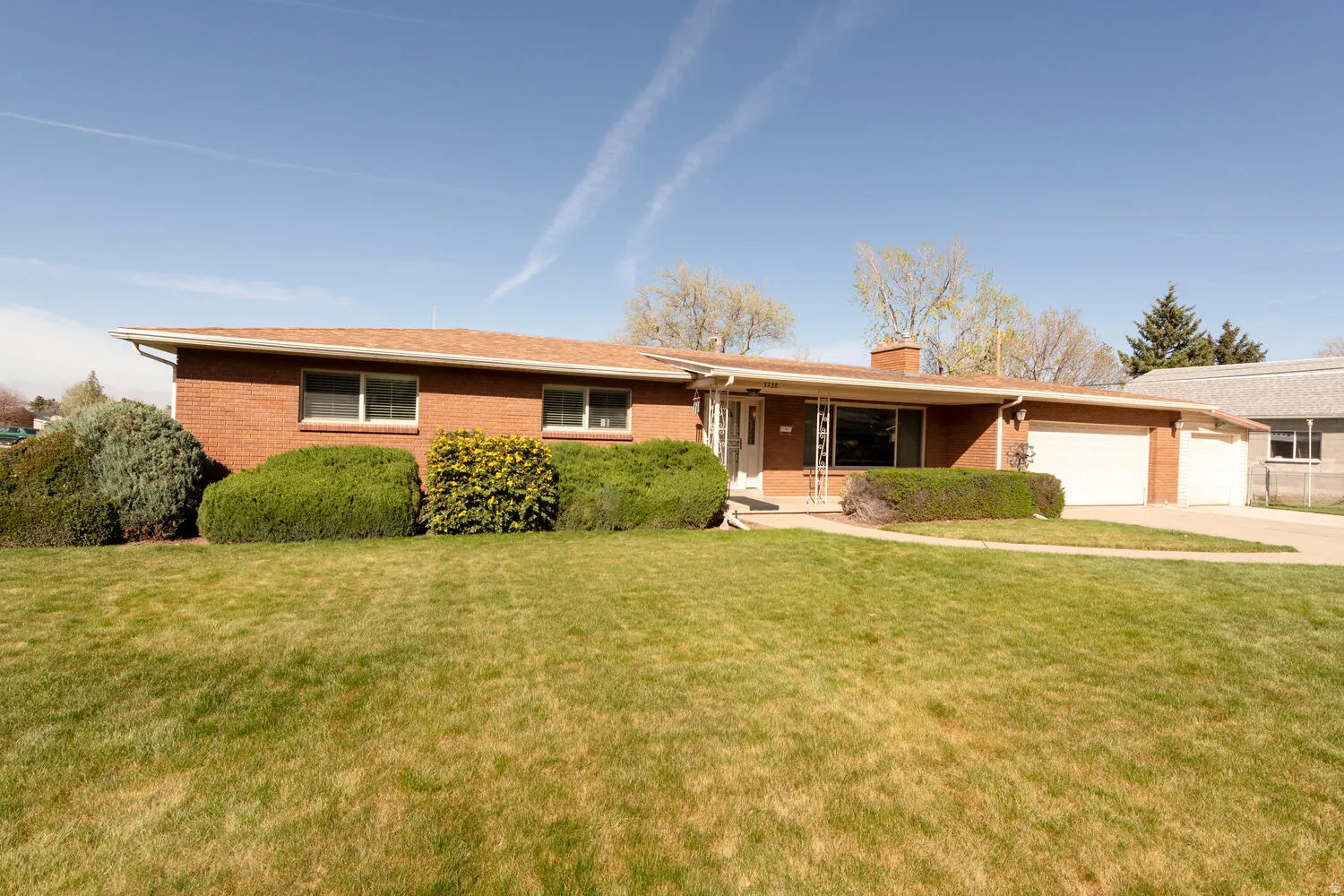 Ranch-style house featuring a front yard, brick siding, an attached garage, a chimney, and driveway