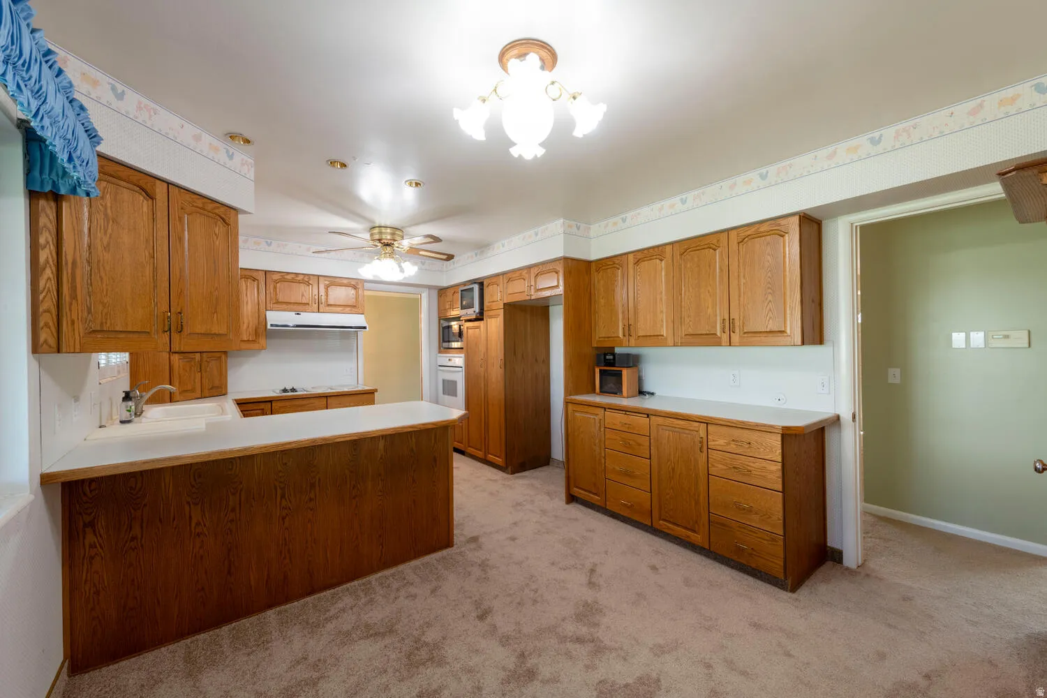 Kitchen with light countertops, a peninsula, wood finish cabinetry, light colored carpet, and white oven