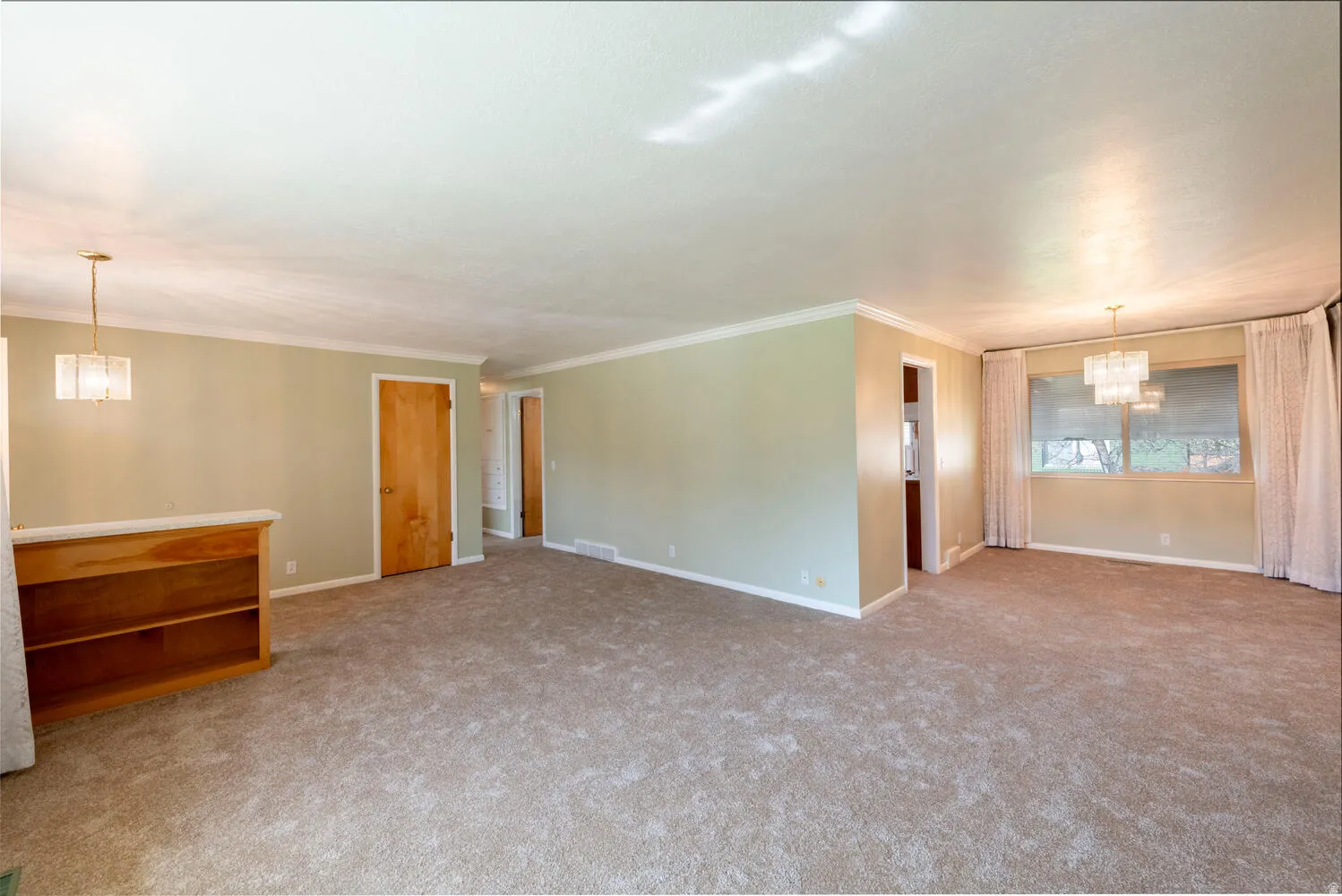 Empty room with hanging lights, light colored carpet, and ornamental molding