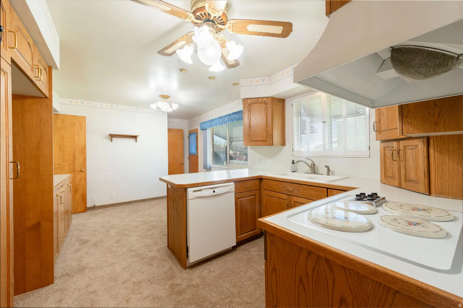 Kitchen with a peninsula, white appliances, exhaust hood, light countertops, and a ceiling fan