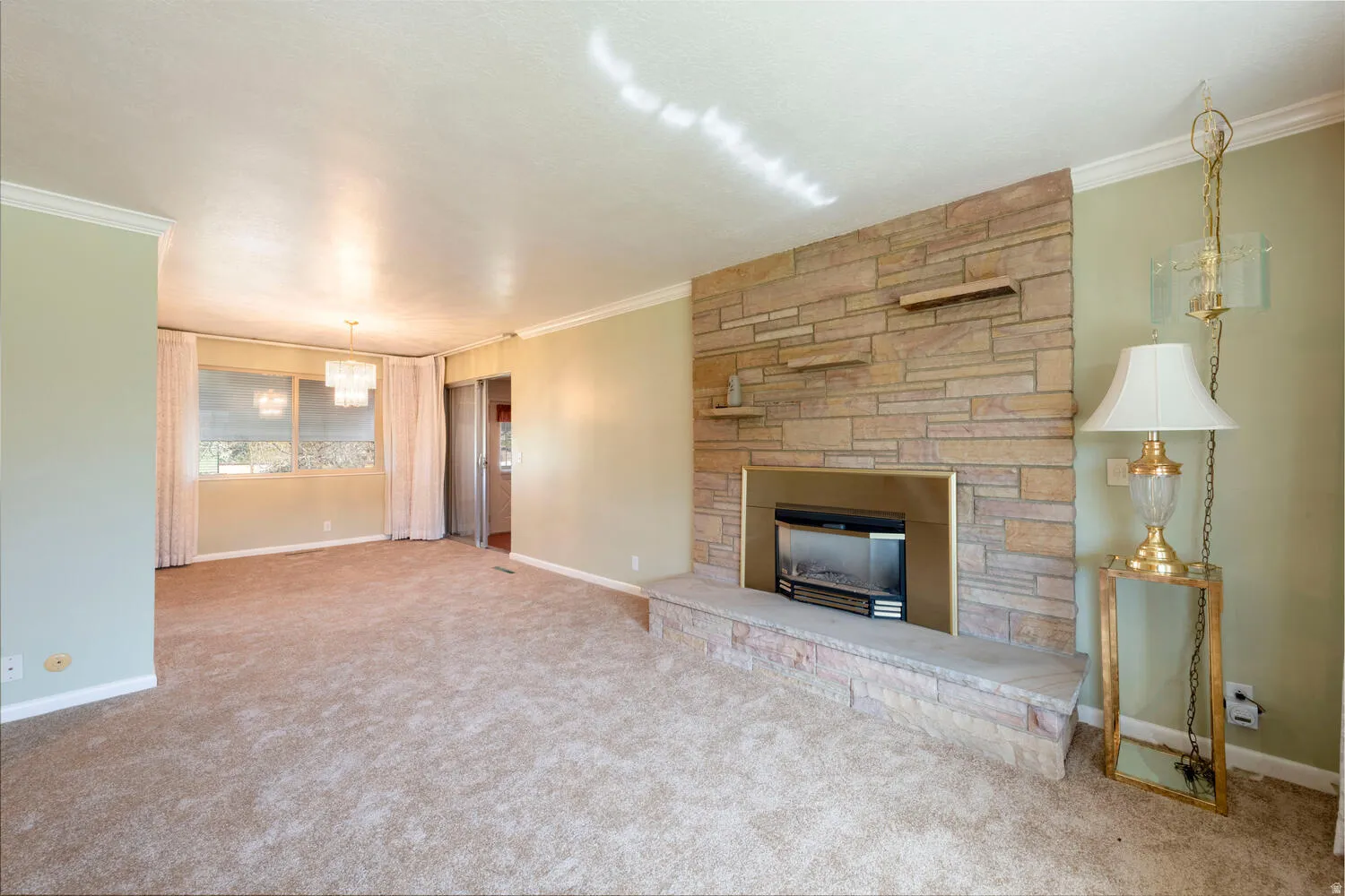 Unfurnished living room featuring ornamental molding, carpet floors, and a stone fireplace