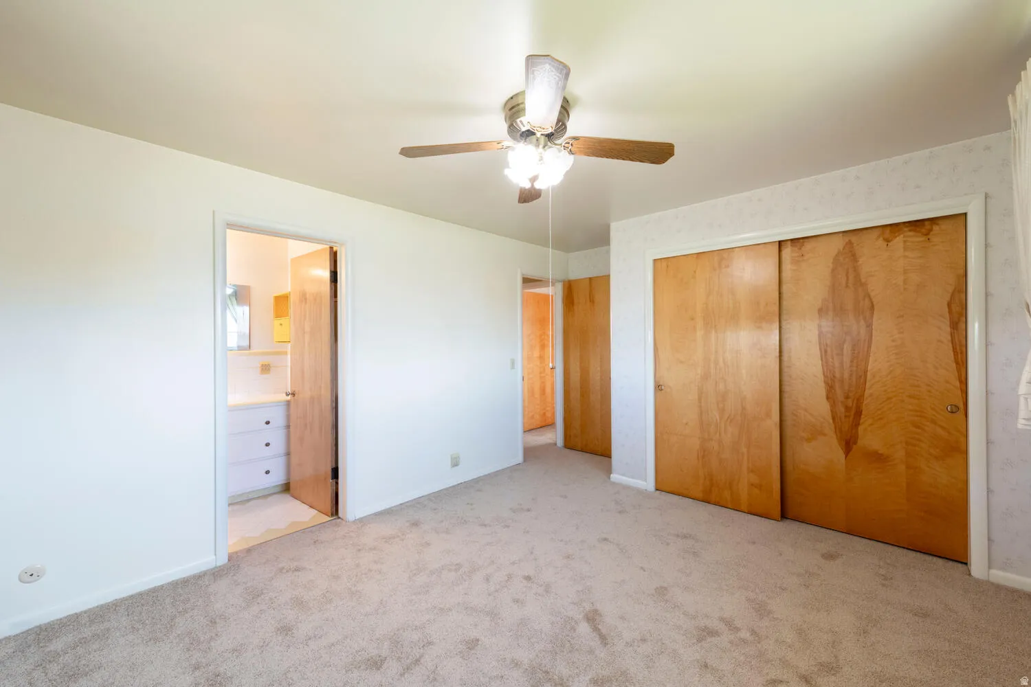 Unfurnished bedroom with light colored carpet, a ceiling fan, connected bathroom, and a closet