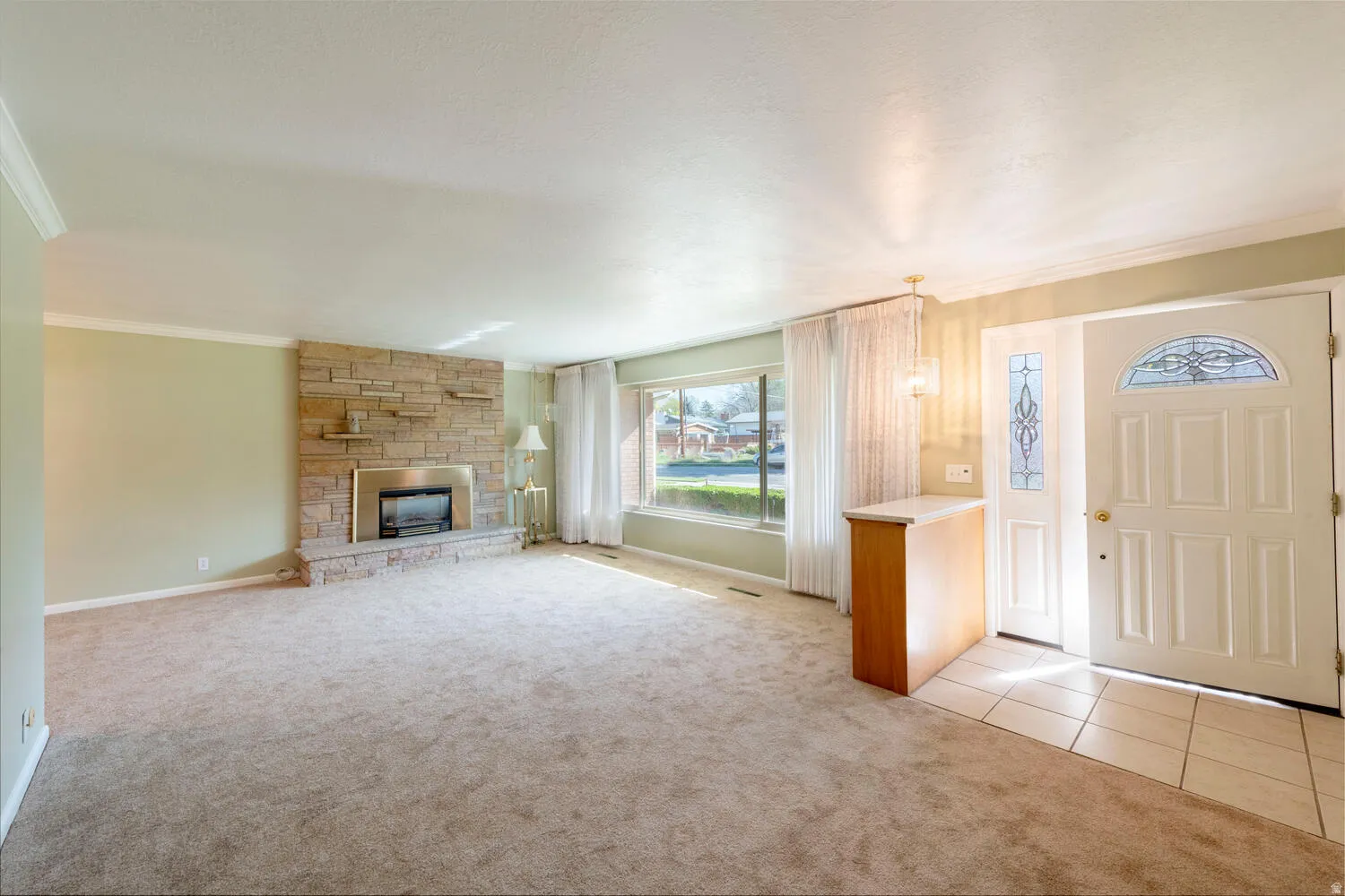 Entrance foyer featuring crown molding, light carpet, a stone fireplace, and light tile patterned flooring
