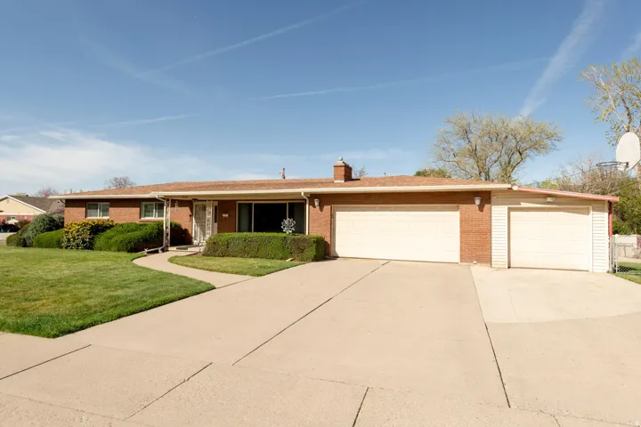 Ranch-style home with brick siding, an attached garage, concrete driveway, a front yard, and a chimney