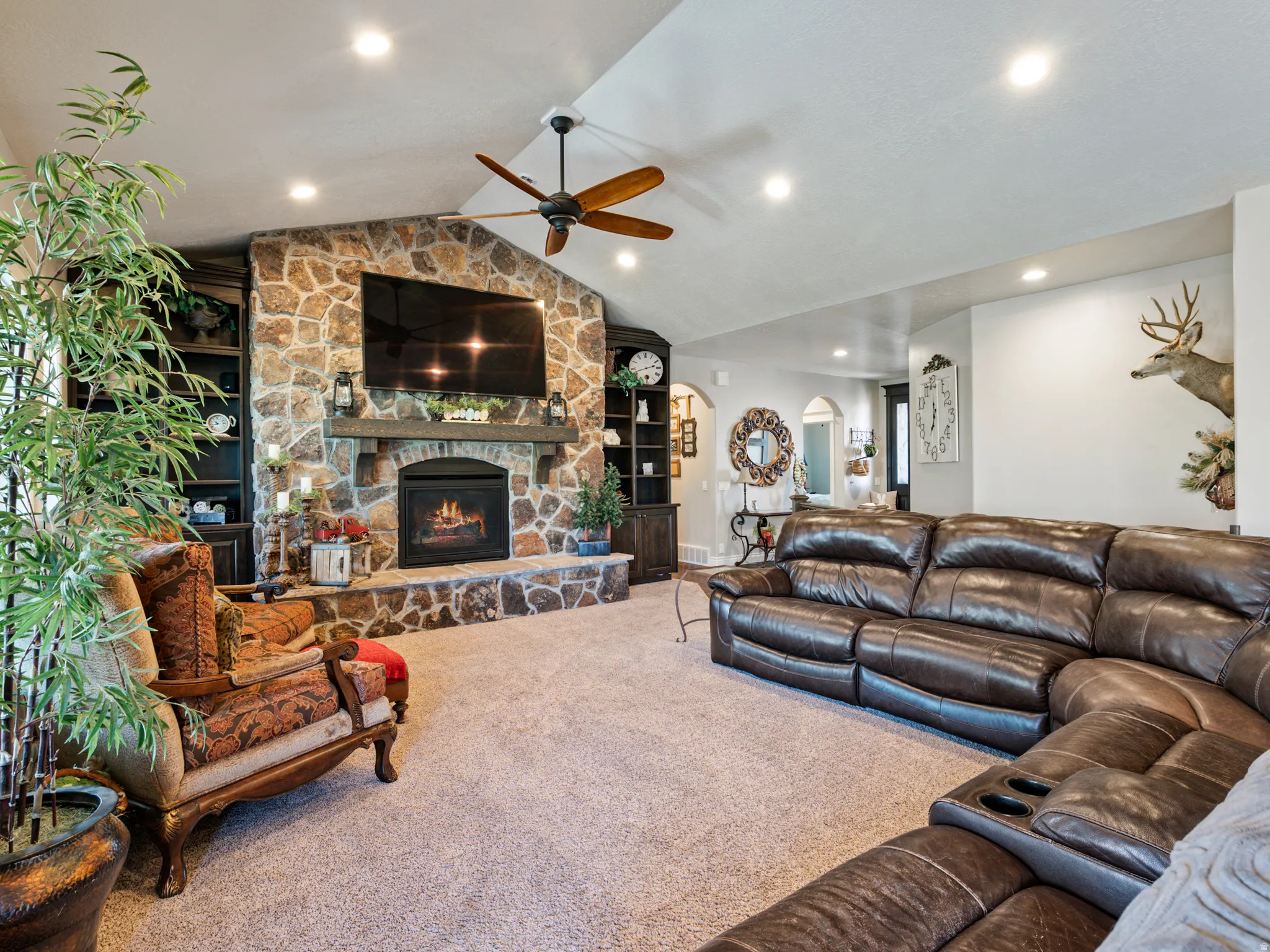 Living area with arched walkways, a ceiling fan, a stone fireplace, carpet floors, and recessed lighting