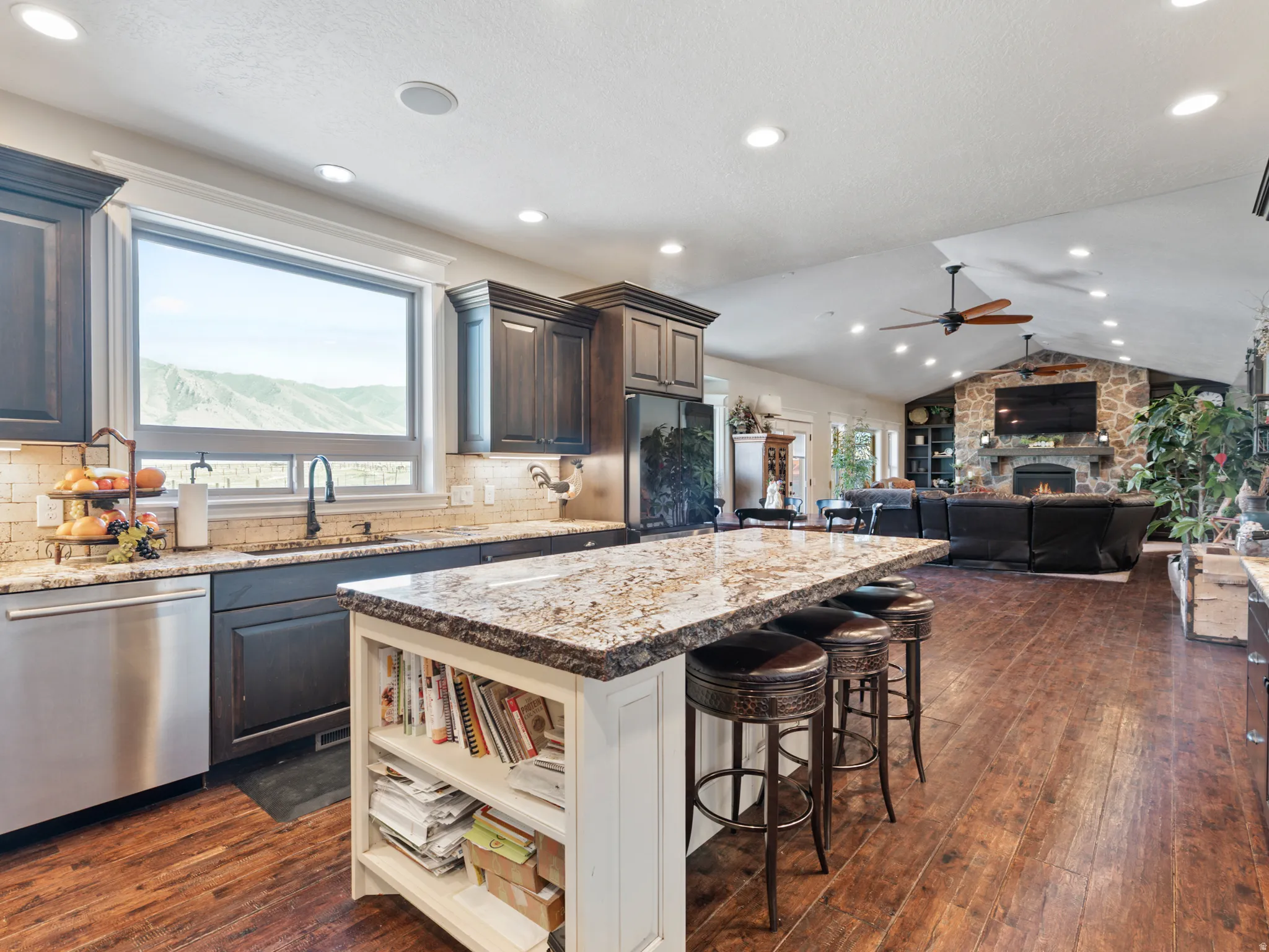 Kitchen featuring open floor plan, tasteful backsplash, a fireplace, lofted ceiling, and light stone countertops