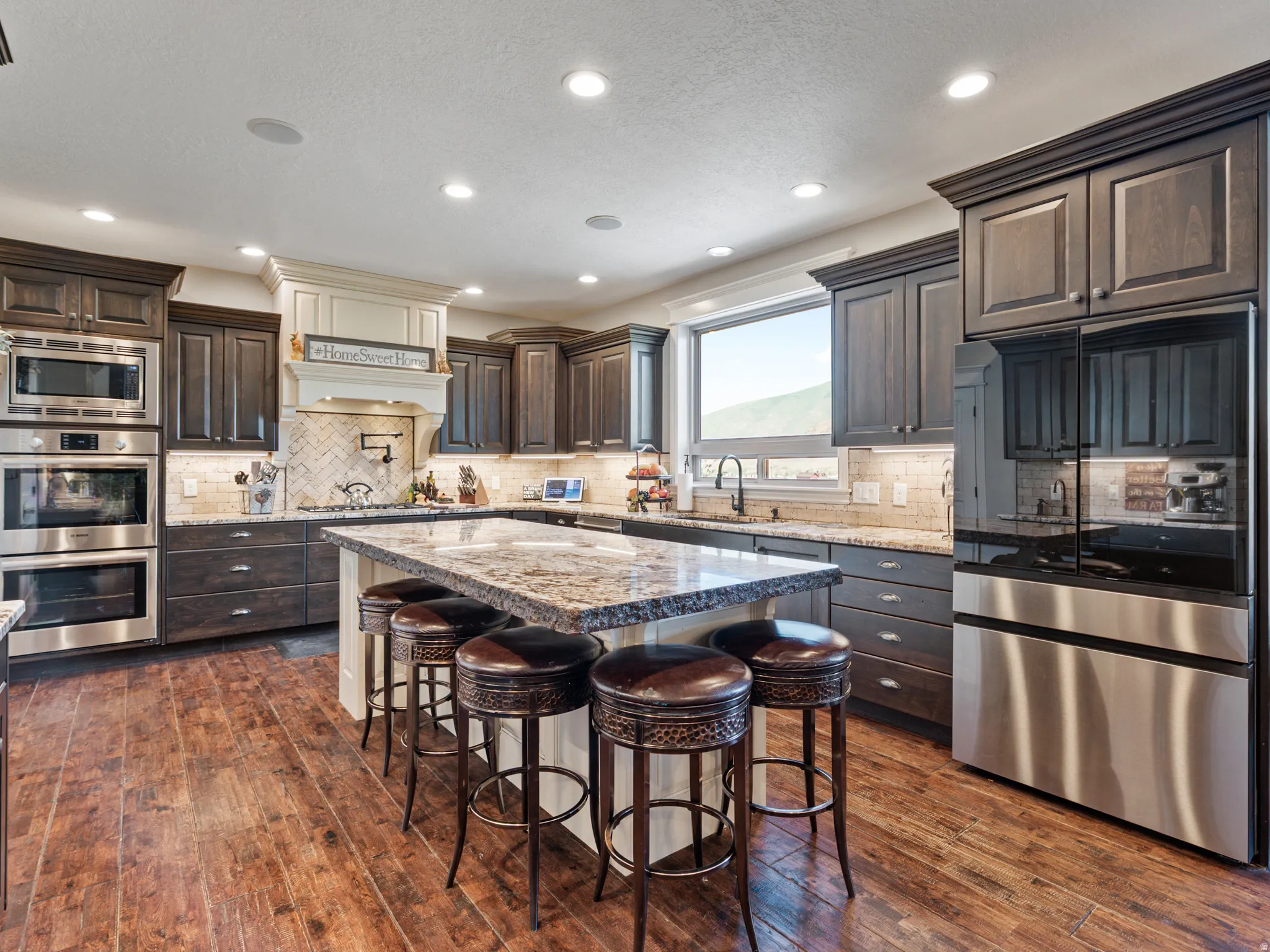 Kitchen featuring stainless steel appliances, dark wood finish cabinetry, light stone counters, a center island, and a kitchen bar