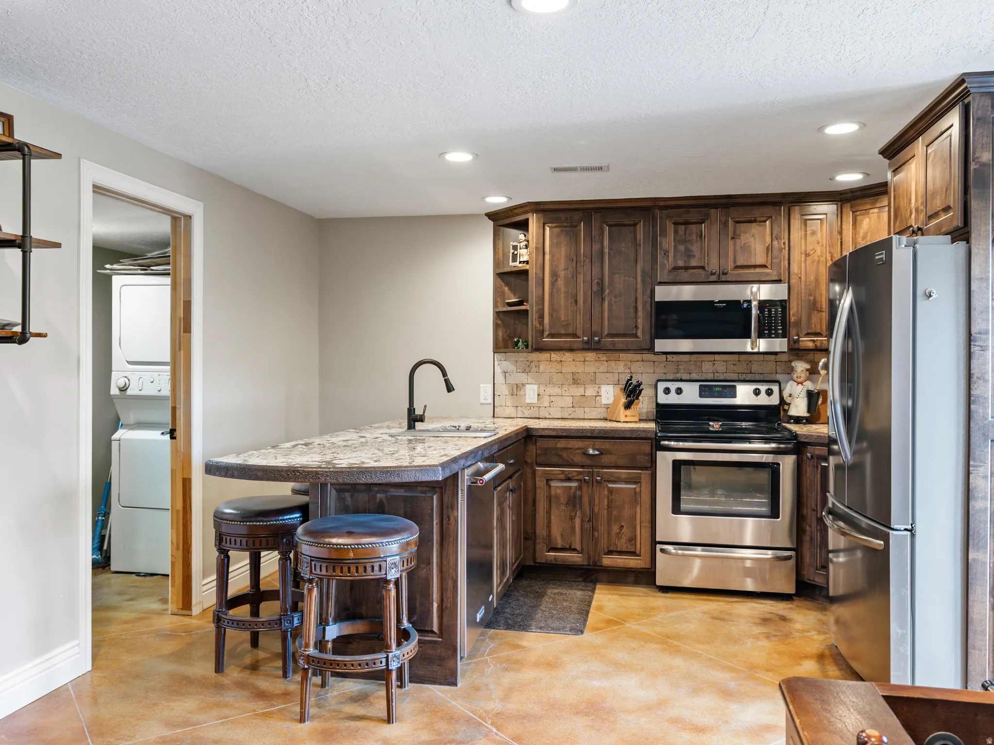 Kitchen featuring open shelves, stainless steel appliances, a kitchen bar, a peninsula, and finished concrete flooring