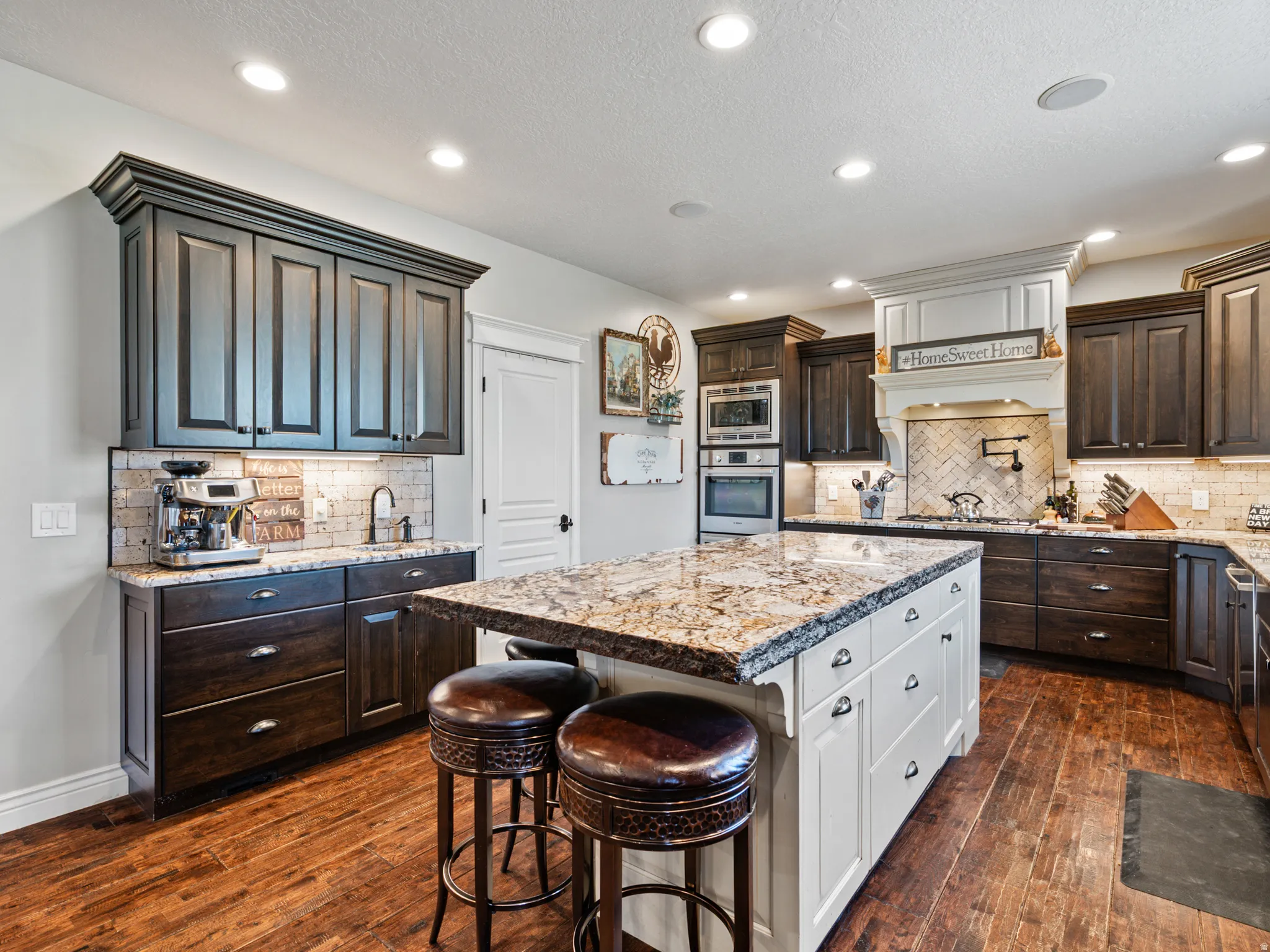 Dual tone kitchen featuring light stone countertops, two tone cabinetry, a kitchen breakfast bar, stainless steel appliances, and dark wood finished floors