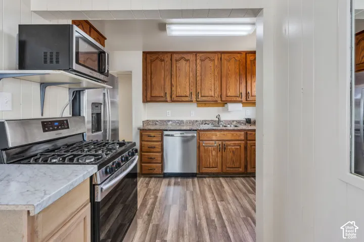 Kitchen featuring wood-finish flooring, wood cabinetry, stone-finish countertops, stainless steel appliances, and ceiling-mounted fluorescent lighting