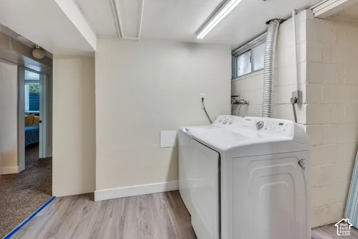 Dedicated laundry area featuring wood-finish flooring, white walls, exposed block foundation, and a utility window