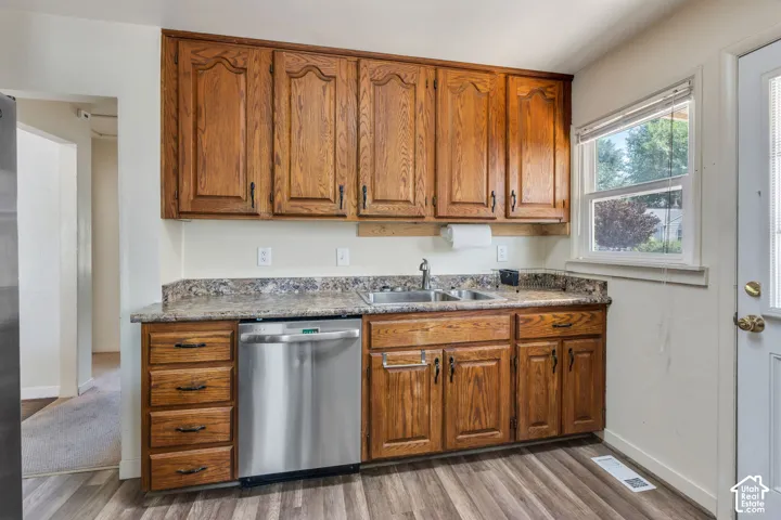 Kitchen featuring wood cabinetry, stainless steel dishwasher, dual basin sink, laminate countertops, and wood-finish flooring
