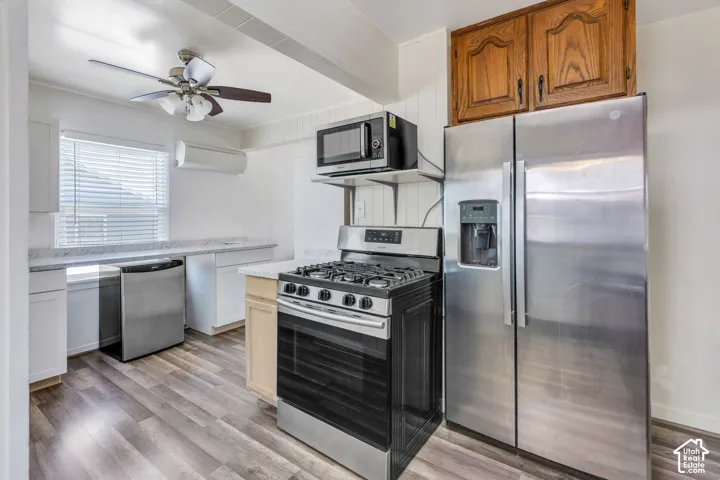 Kitchen featuring stainless steel appliances, wood-finish flooring, white cabinetry, light countertops, and a ceiling fan