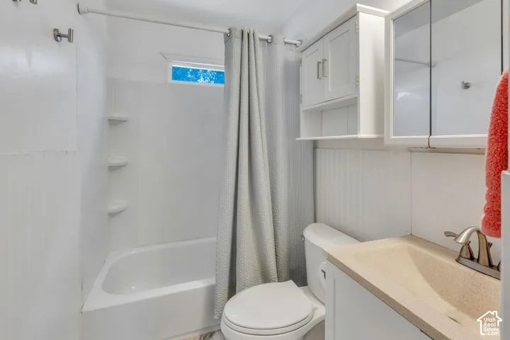 White bathroom featuring a built-in tub with shelving, a toilet, and a vanity with an integrated sink