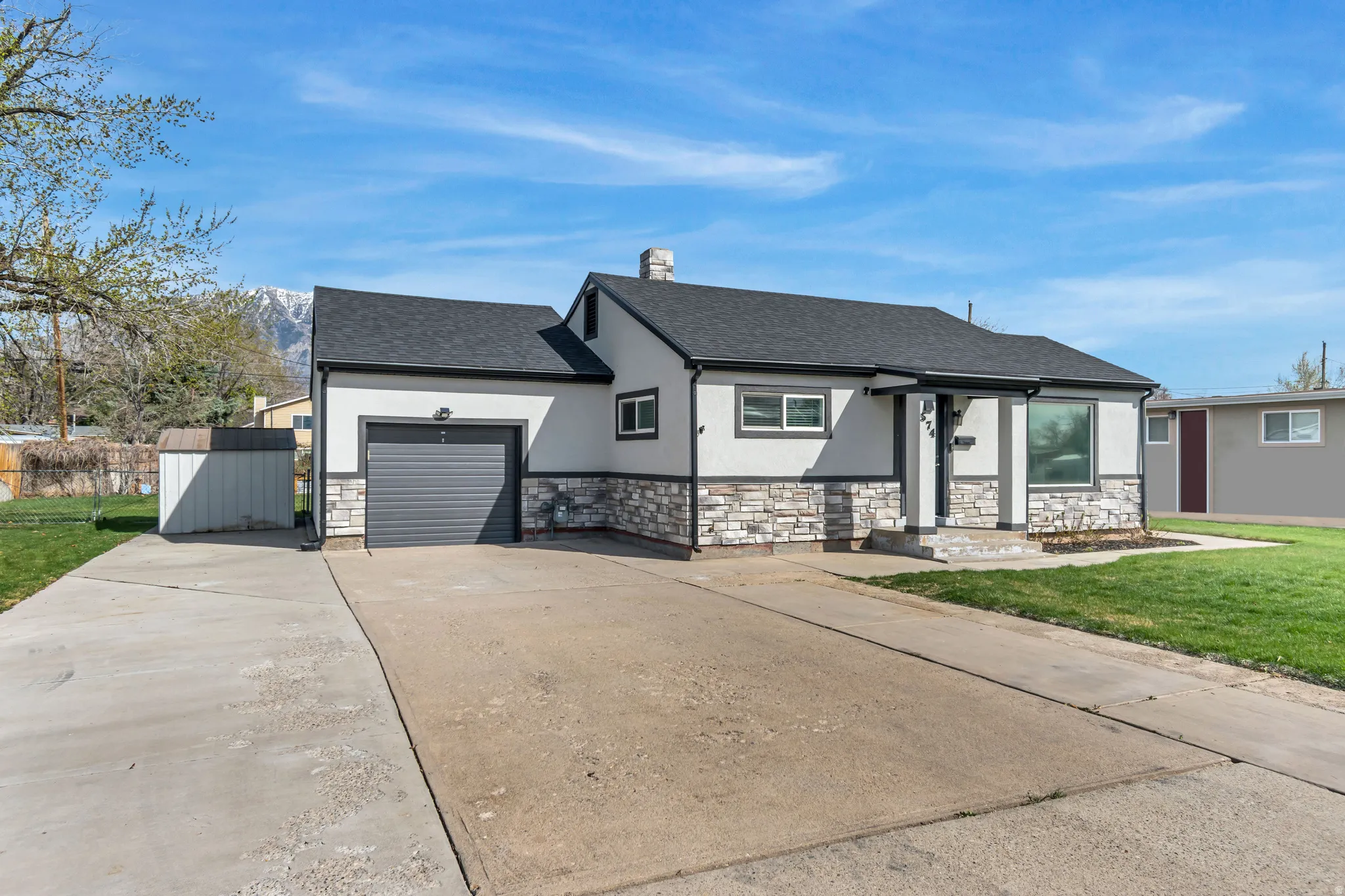 View of front facade with concrete driveway, stone siding, stucco siding, and a shingled roof