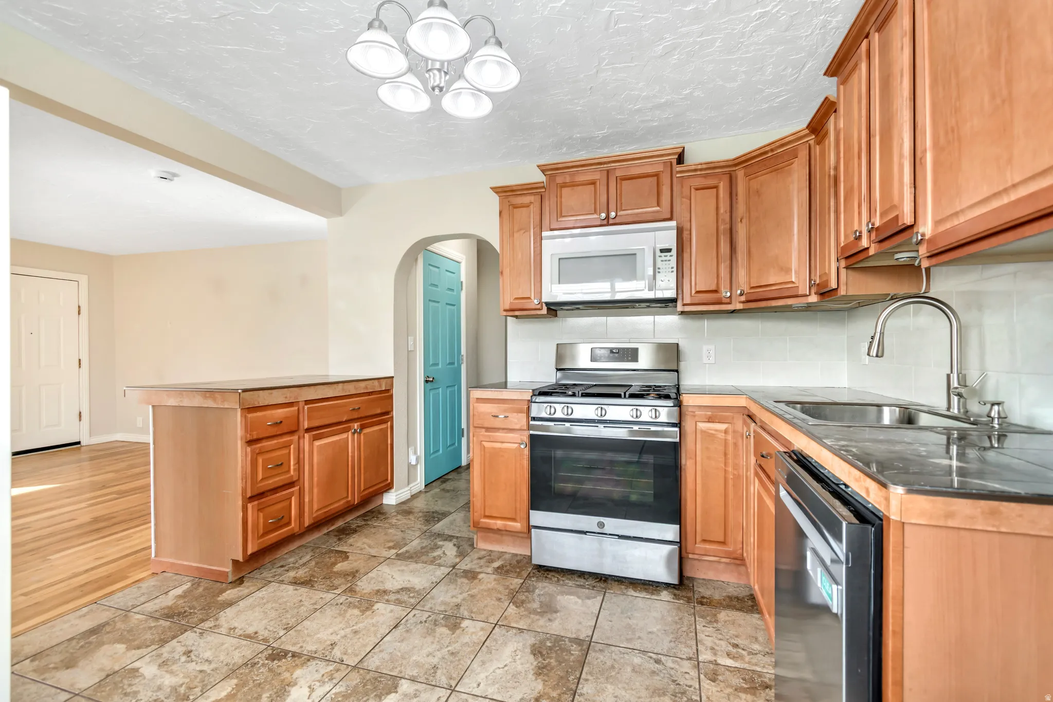 Kitchen featuring arched walkways, stainless steel appliances, backsplash, a peninsula, and a chandelier