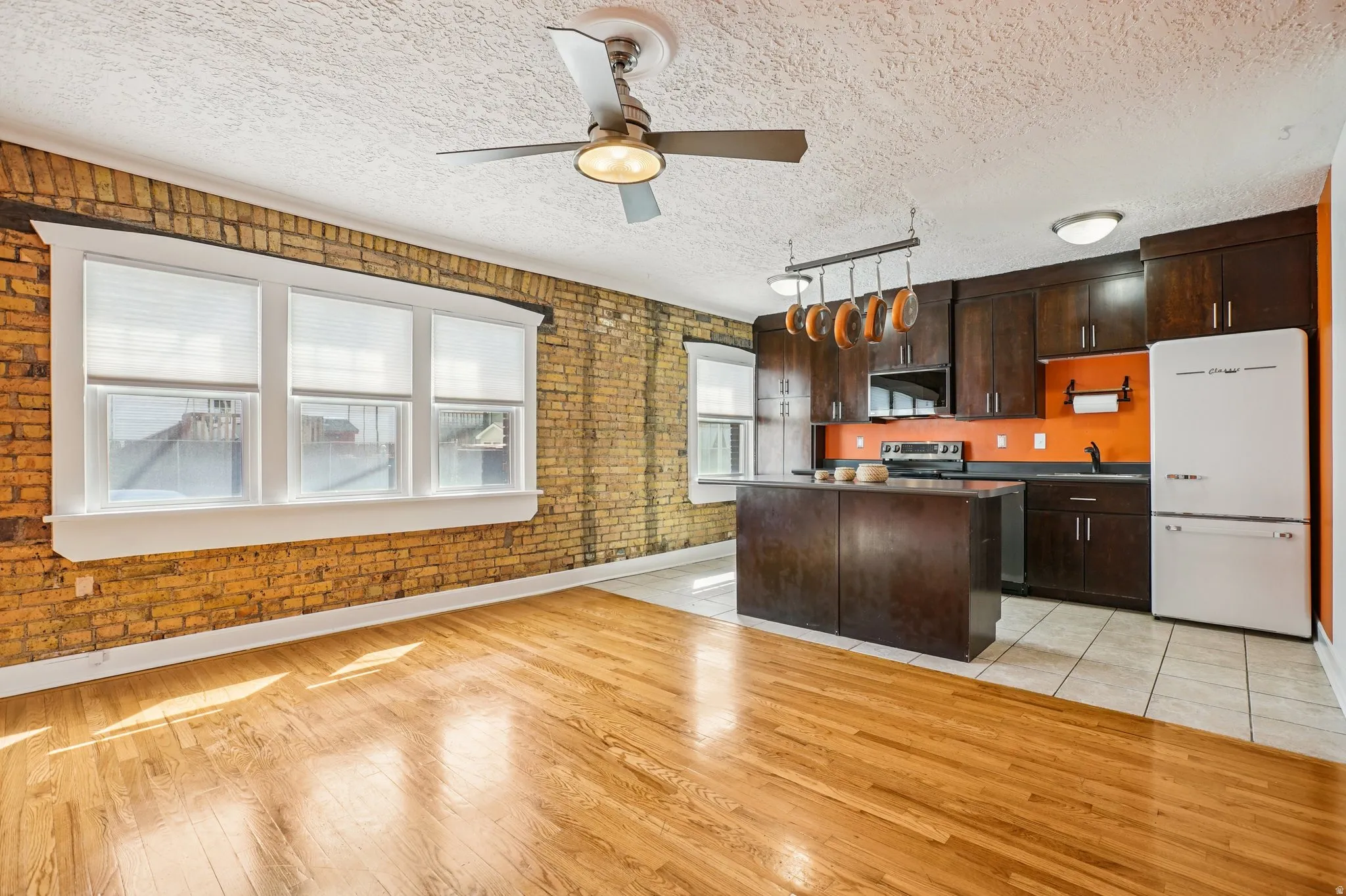 Kitchen with stainless steel appliances, dark wood finish cabinets, dark countertops, brick wall, and a kitchen island