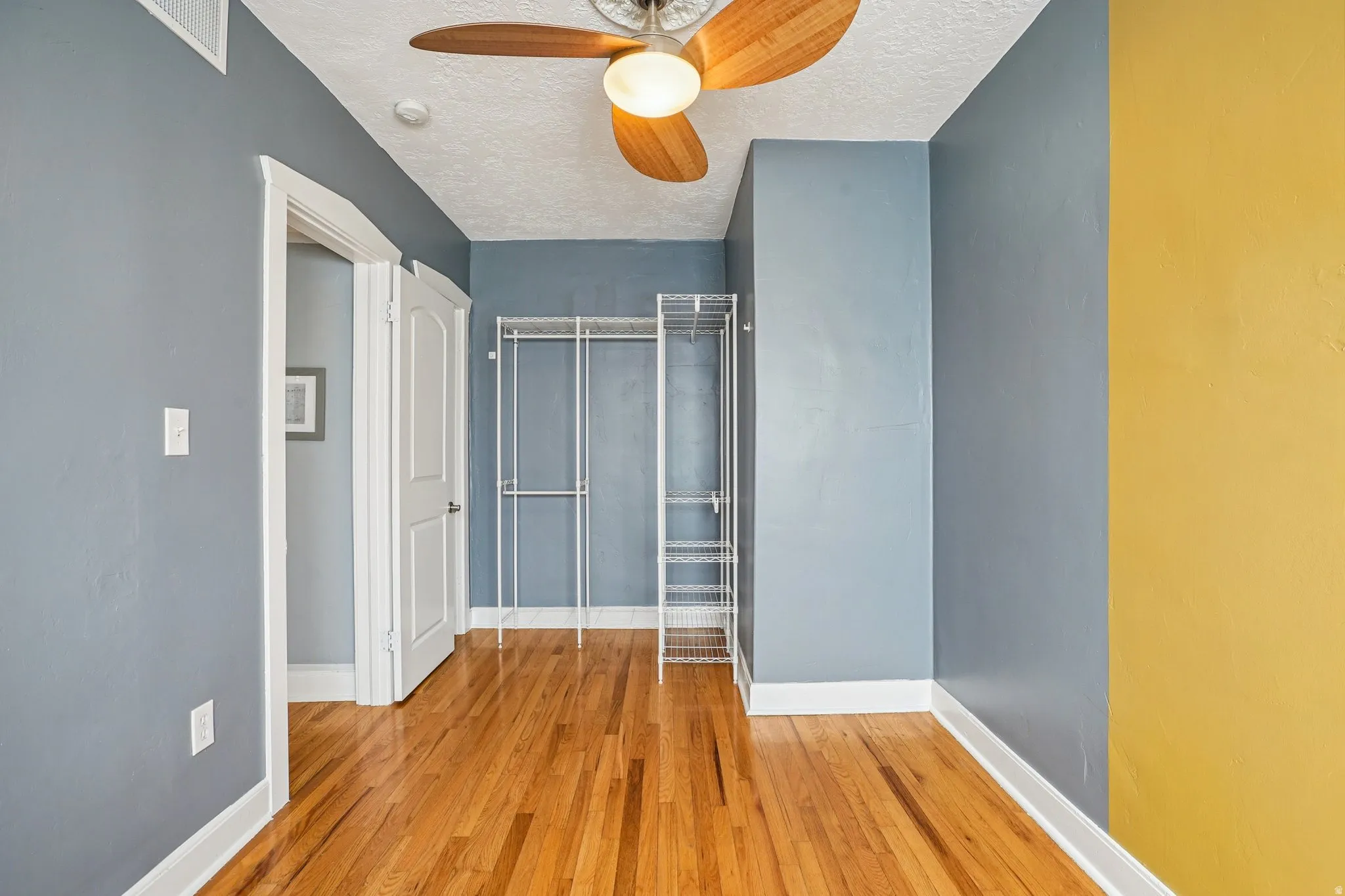 Unfurnished bedroom featuring a closet, light wood-type flooring, a textured ceiling, and a ceiling fan