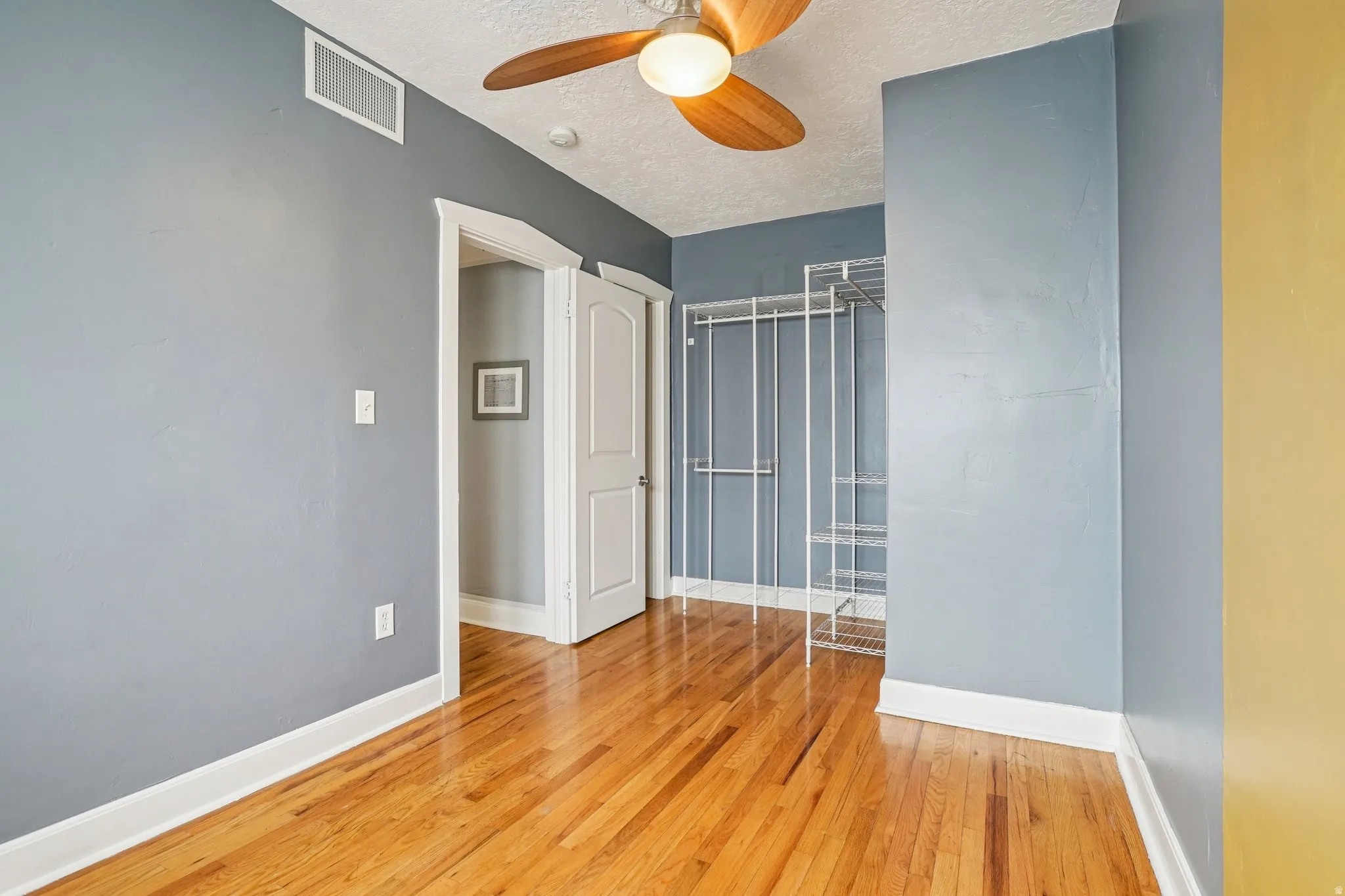 Empty room featuring light wood finished floors, a ceiling fan, and a textured ceiling