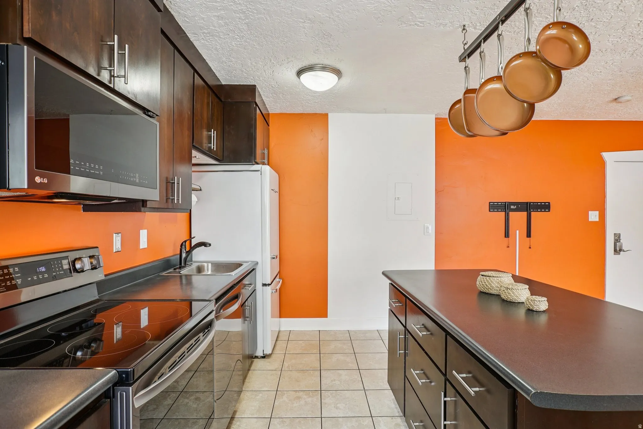 Kitchen featuring dark countertops, stainless steel appliances, dark wood finish cabinets, a textured ceiling, and a kitchen island