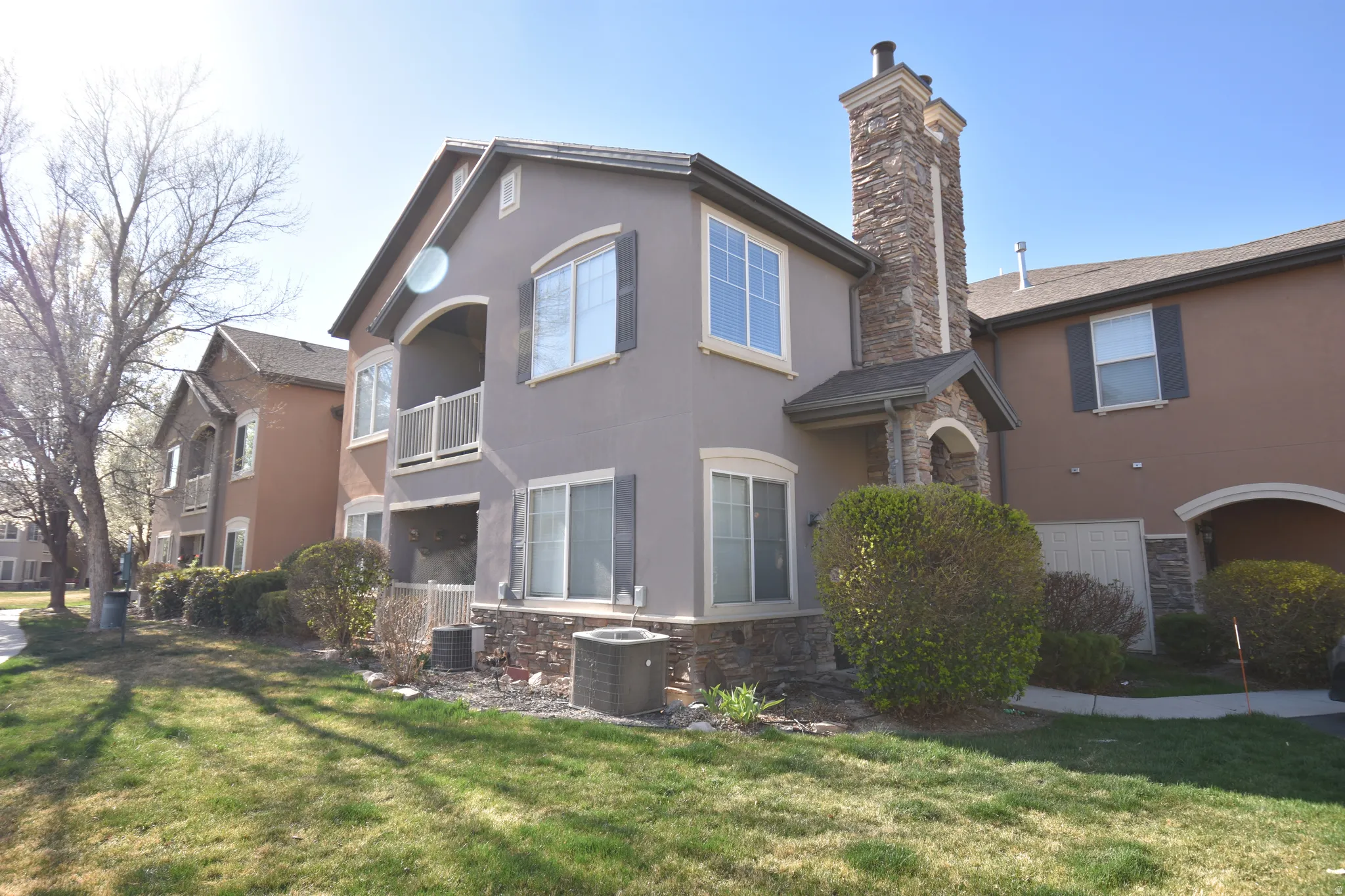 Back of house with stone siding, stucco siding, a lawn, a chimney, and a balcony