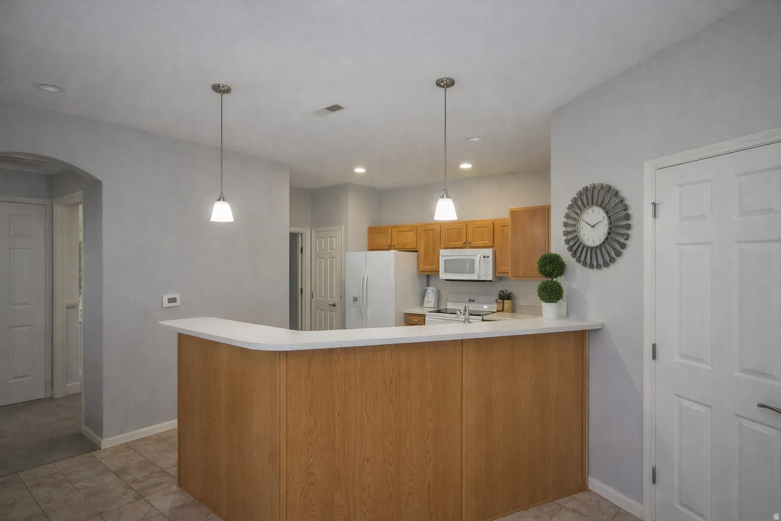 Kitchen featuring light countertops, a peninsula, arched walkways, decorative backsplash, and pendant lighting