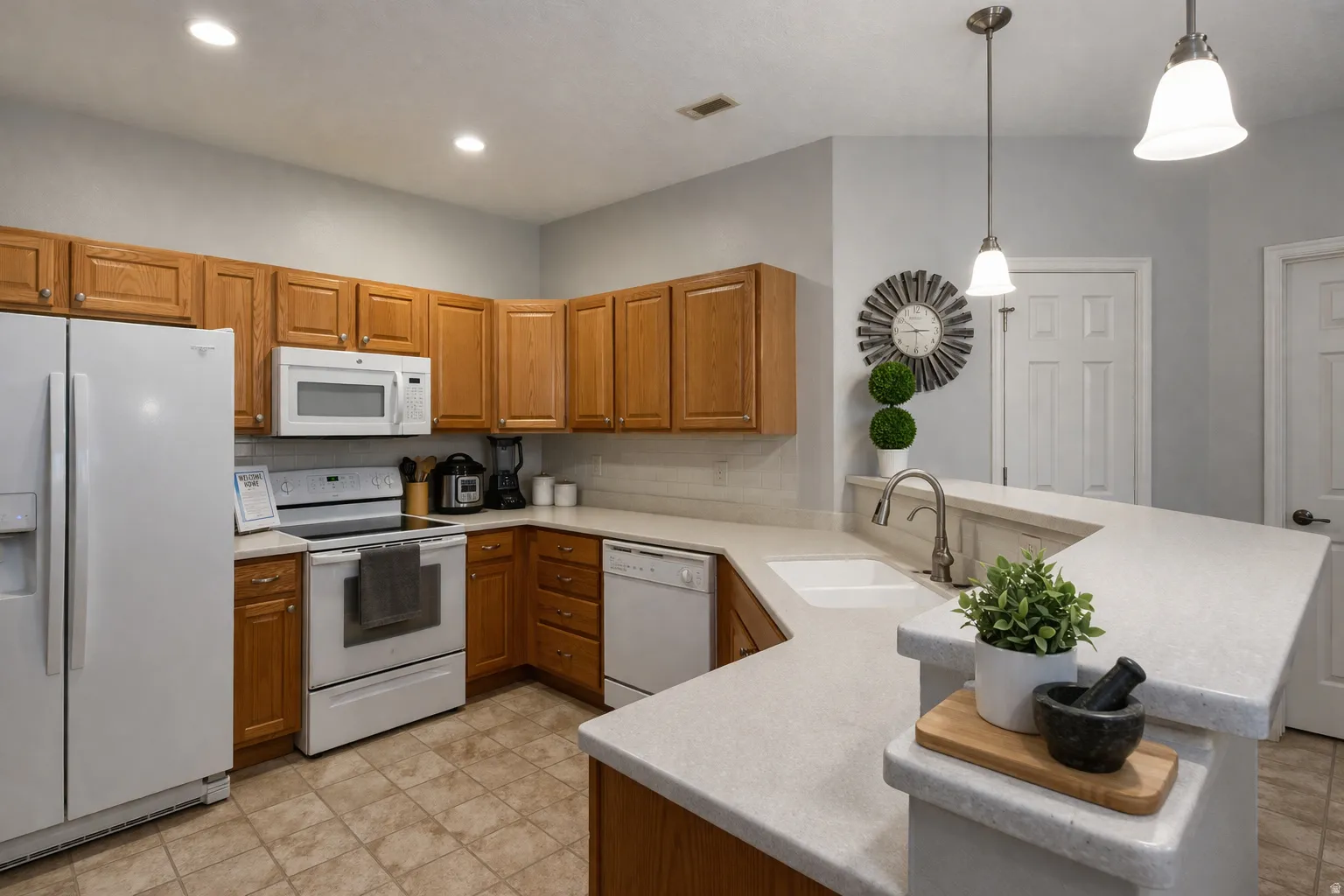 Kitchen with white appliances, a peninsula, wood finish cabinets, and hanging light fixtures