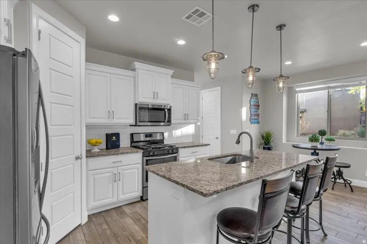 Kitchen with stainless steel appliances, a kitchen island with sink, white cabinets, and light wood finished floors