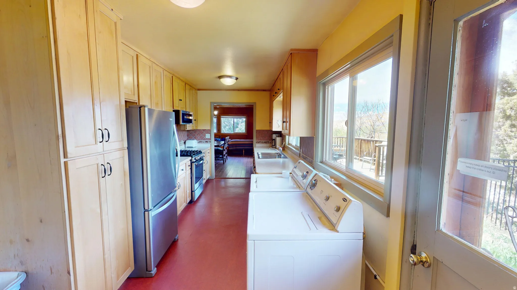 Kitchen featuring stainless steel appliances, light countertops, washer and dryer, and light wood finish cabinetry