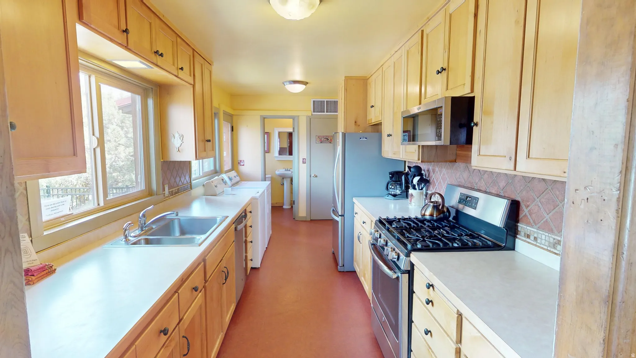 Kitchen with stainless steel appliances, light wood finish cabinetry, light countertops, and tasteful backsplash