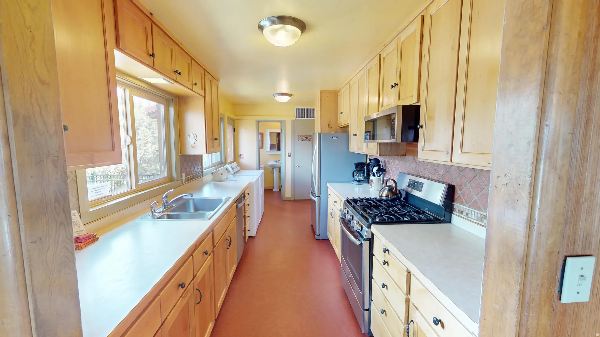 Kitchen with stainless steel appliances, light countertops, light wood finish cabinets, and tasteful backsplash