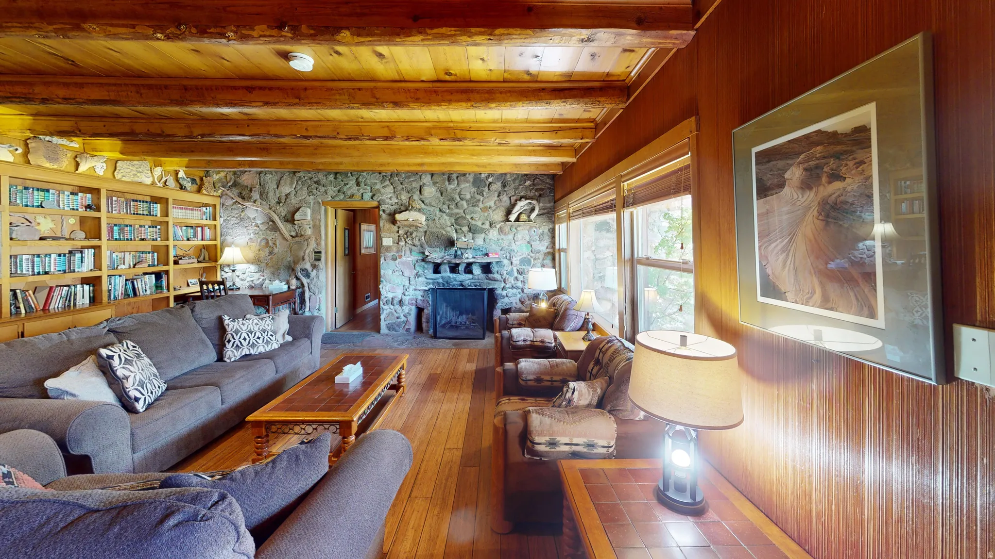 Living area featuring a stone fireplace, hardwood / wood-style floors, and a wooden ceiling with exposed beams