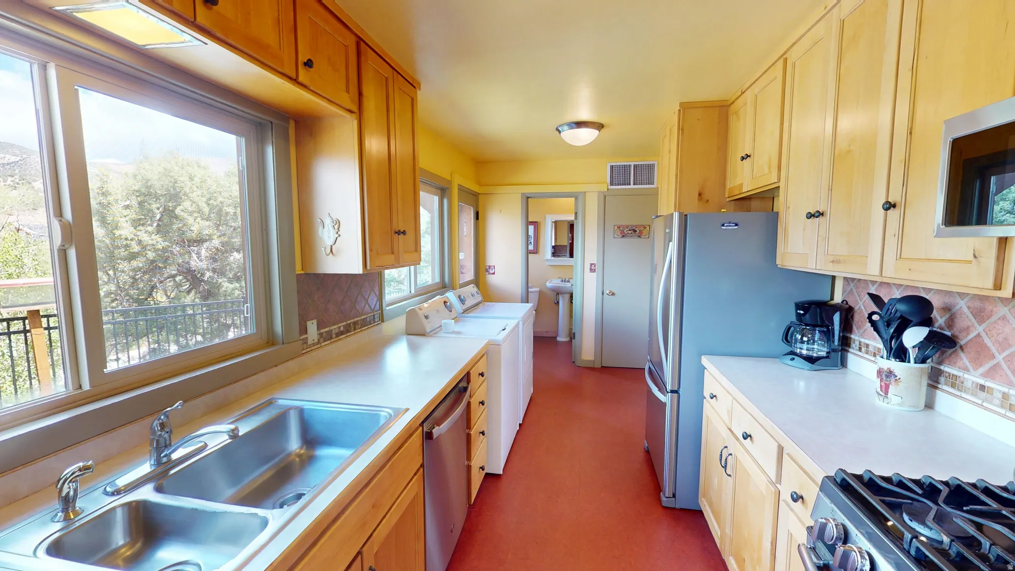 Kitchen featuring tasteful backsplash, independent washer and dryer, light countertops, stainless steel appliances, and light wood finish cabinetry