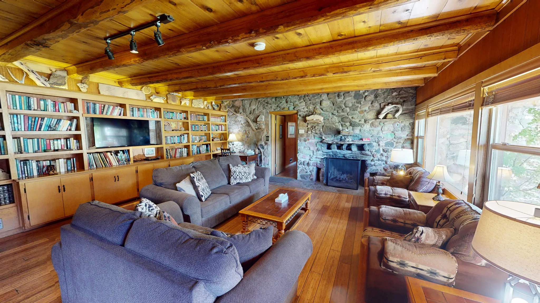 Living area featuring a stone fireplace, hardwood / wood-style floors, and a wooden ceiling with exposed beams