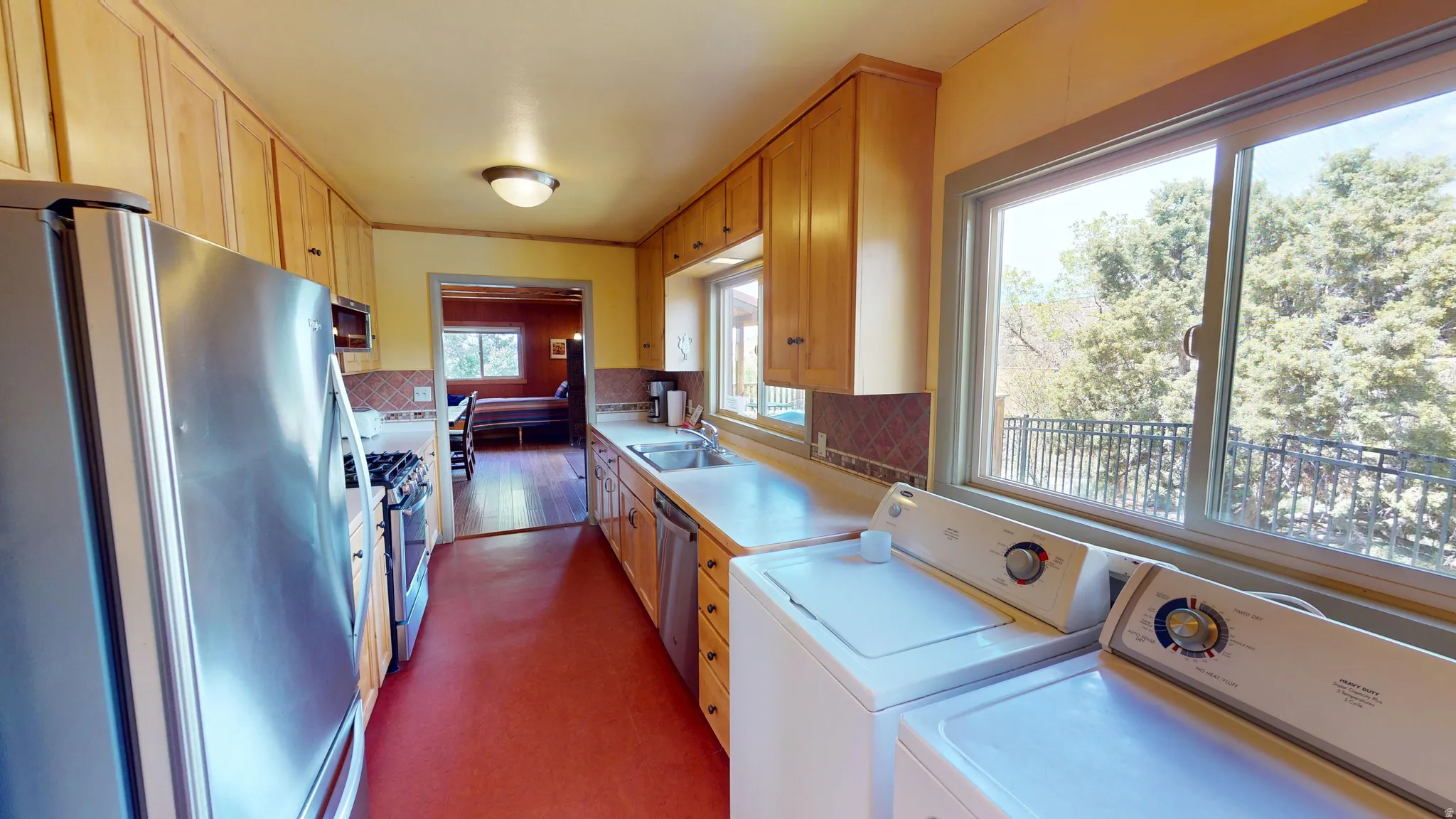 Kitchen with stainless steel appliances, light countertops, washer and dryer, light wood finish cabinets, and dark flooring