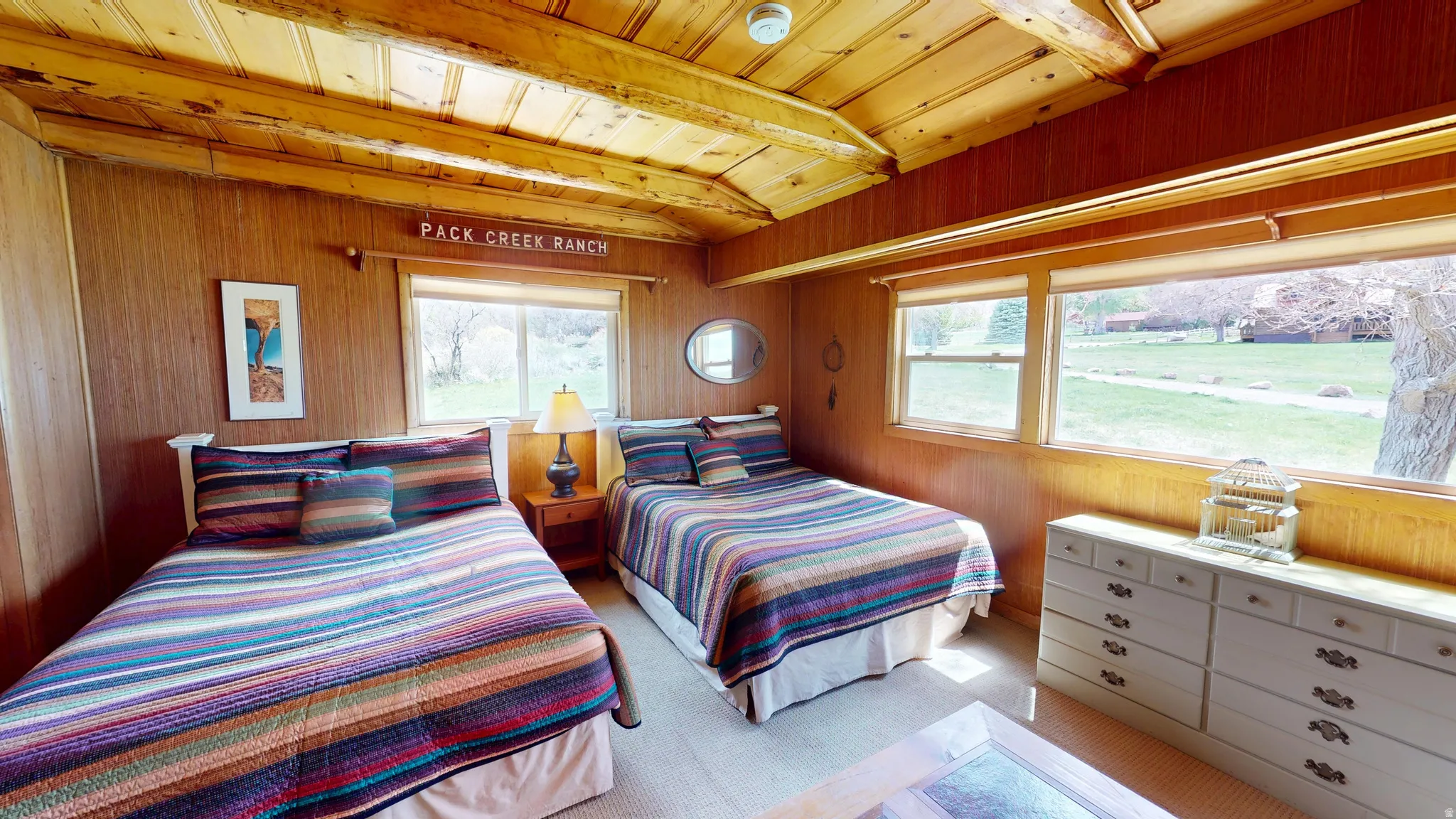 Bedroom with a wooden ceiling with exposed beams, wooden walls, and light colored carpet
