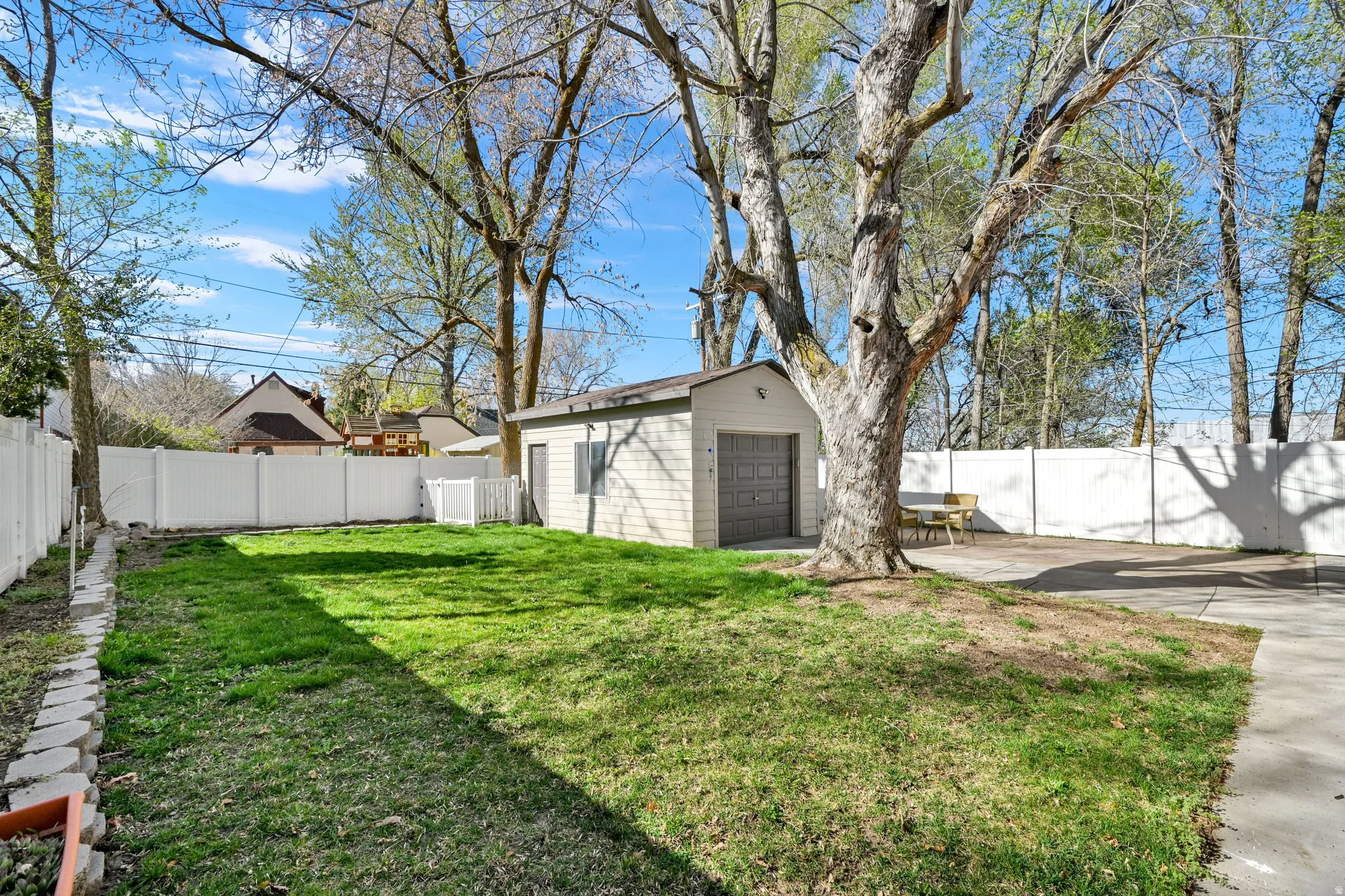 Fenced backyard with detached 1-car garage and driveway/patio space, and mature trees