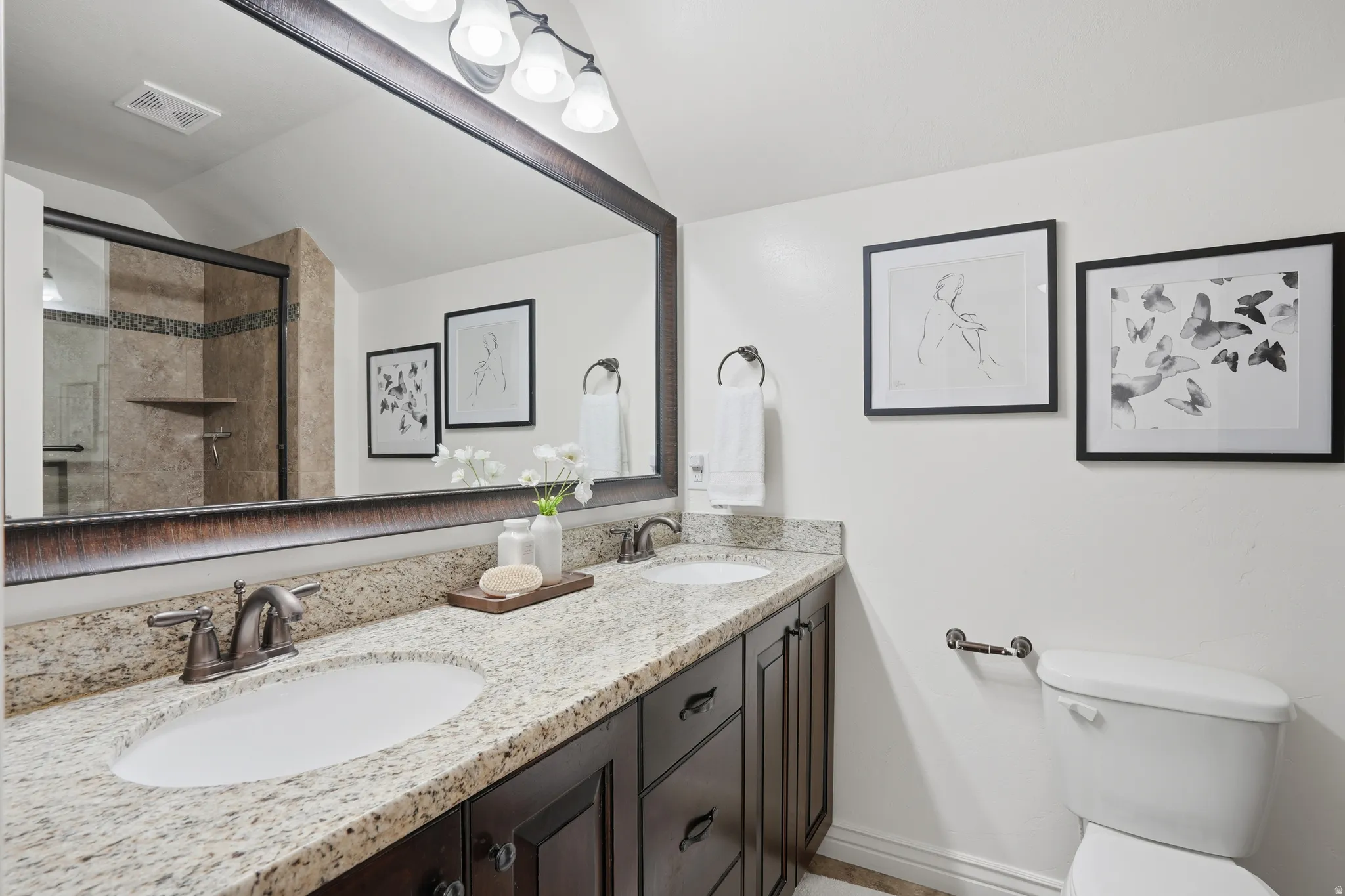 Full bath with double vanity, a shower stall, and lofted ceiling