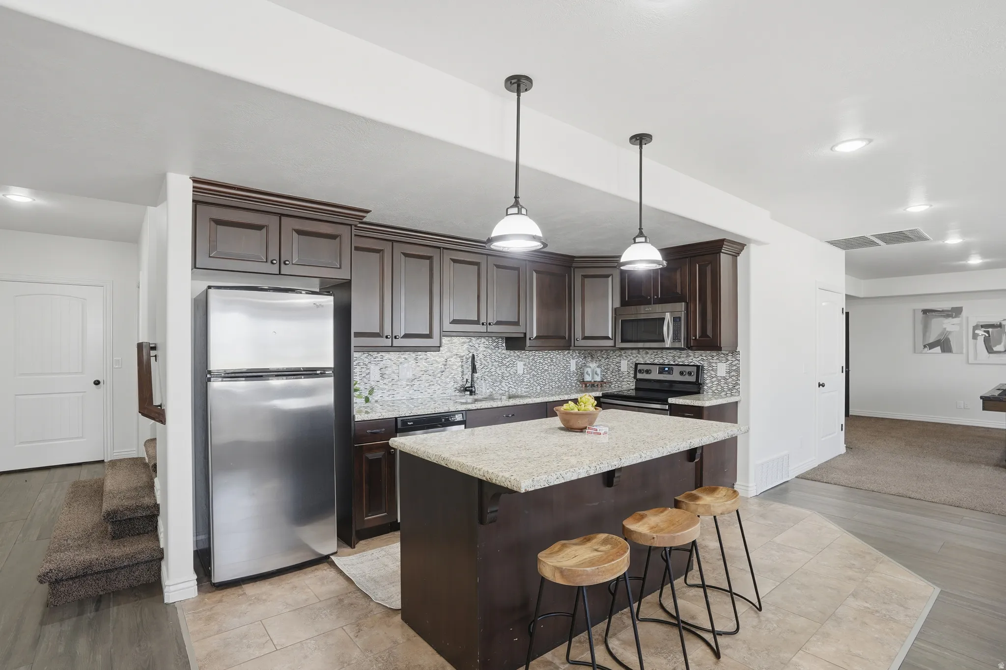 Kitchen featuring stainless steel appliances, dark wood finish cabinets, a kitchen bar, a kitchen island, and light wood-style floors