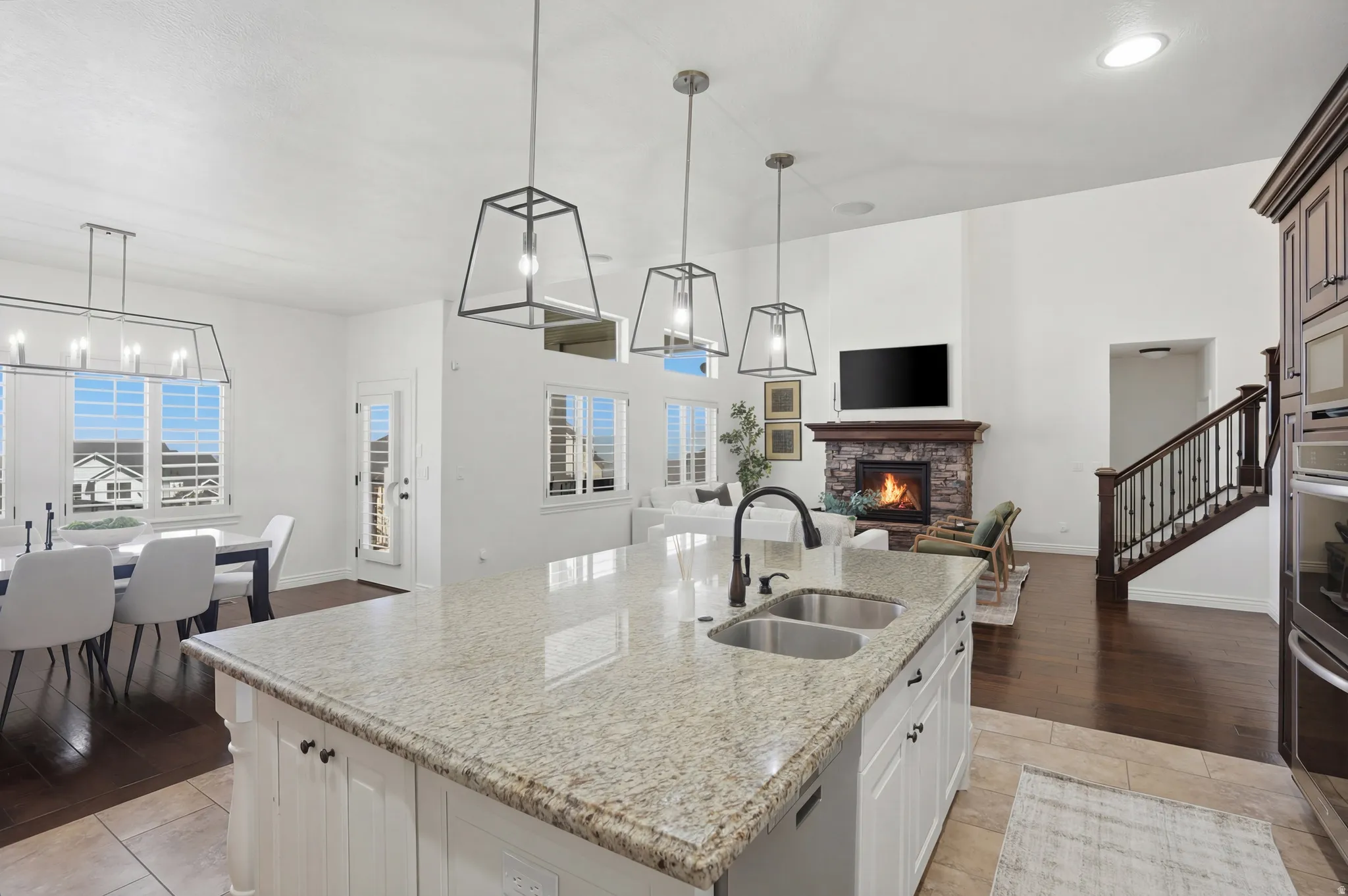 Kitchen with suspended lighting, a center island with sink, open floor plan, light stone counters, and a stone fireplace